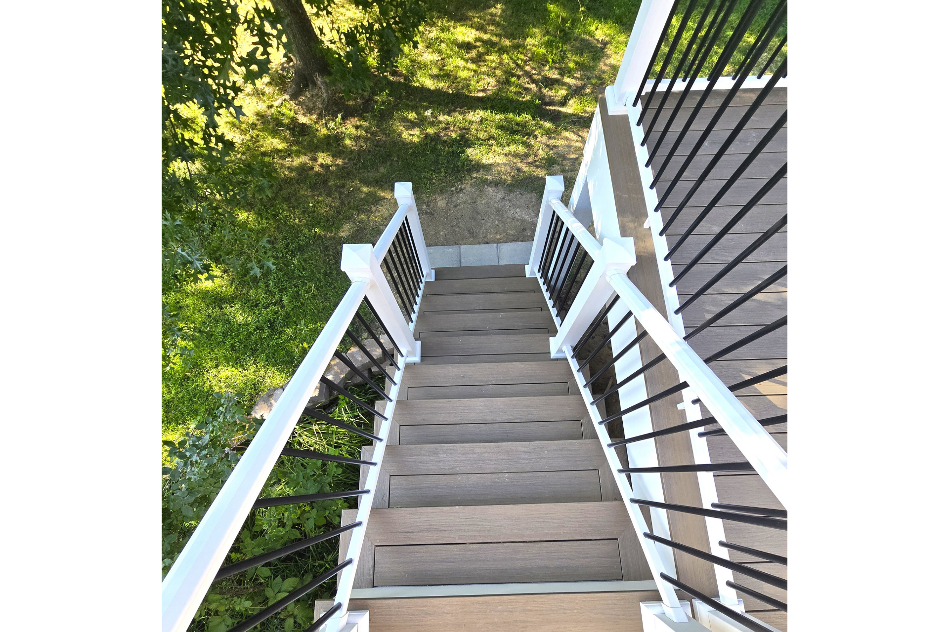 A high-angle view looking down a set of wooden outdoor stairs with white railings and black metal spindles.