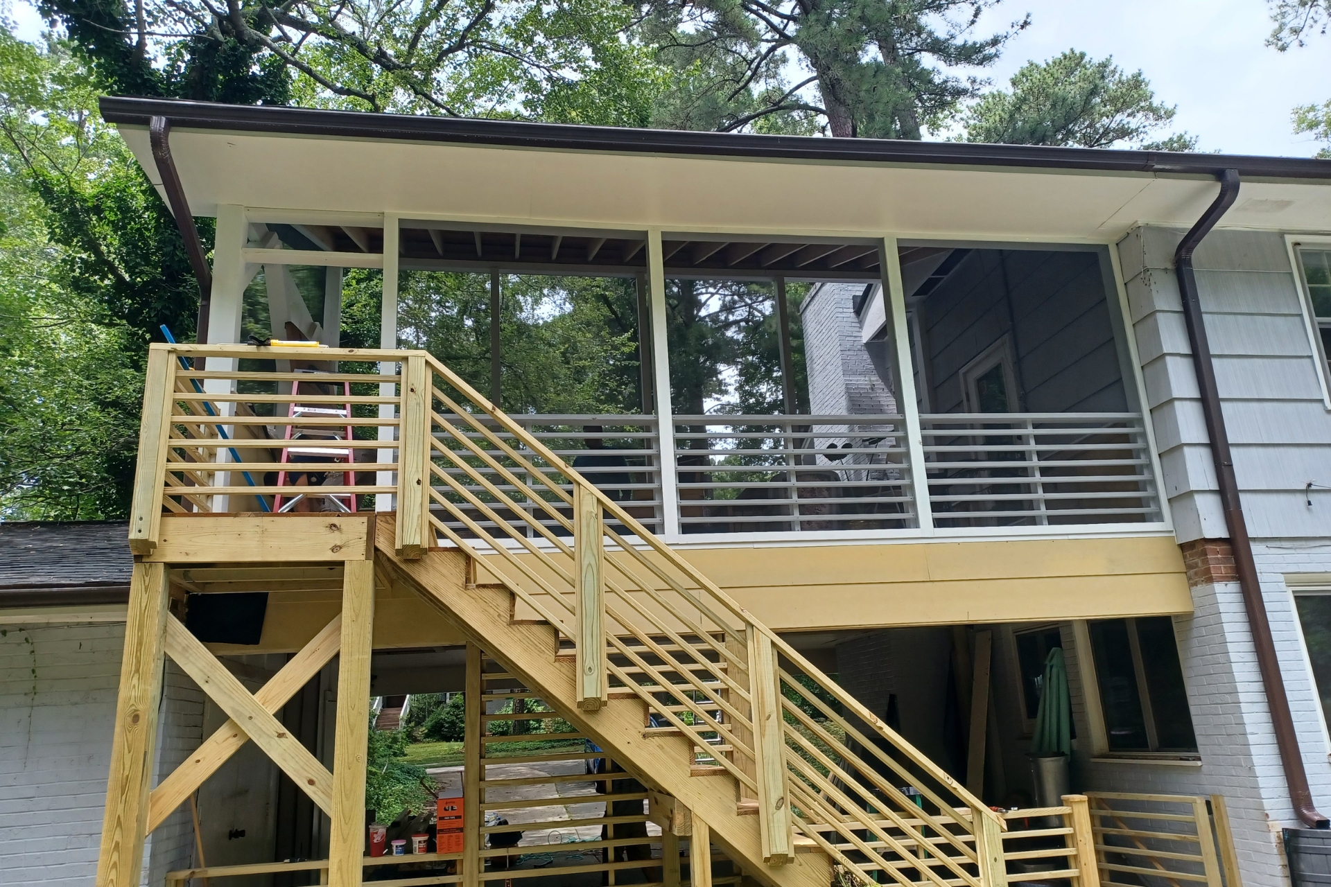A newly built wooden deck with horizontal railings and stairs attached to the side of a house with a screened-in porch.