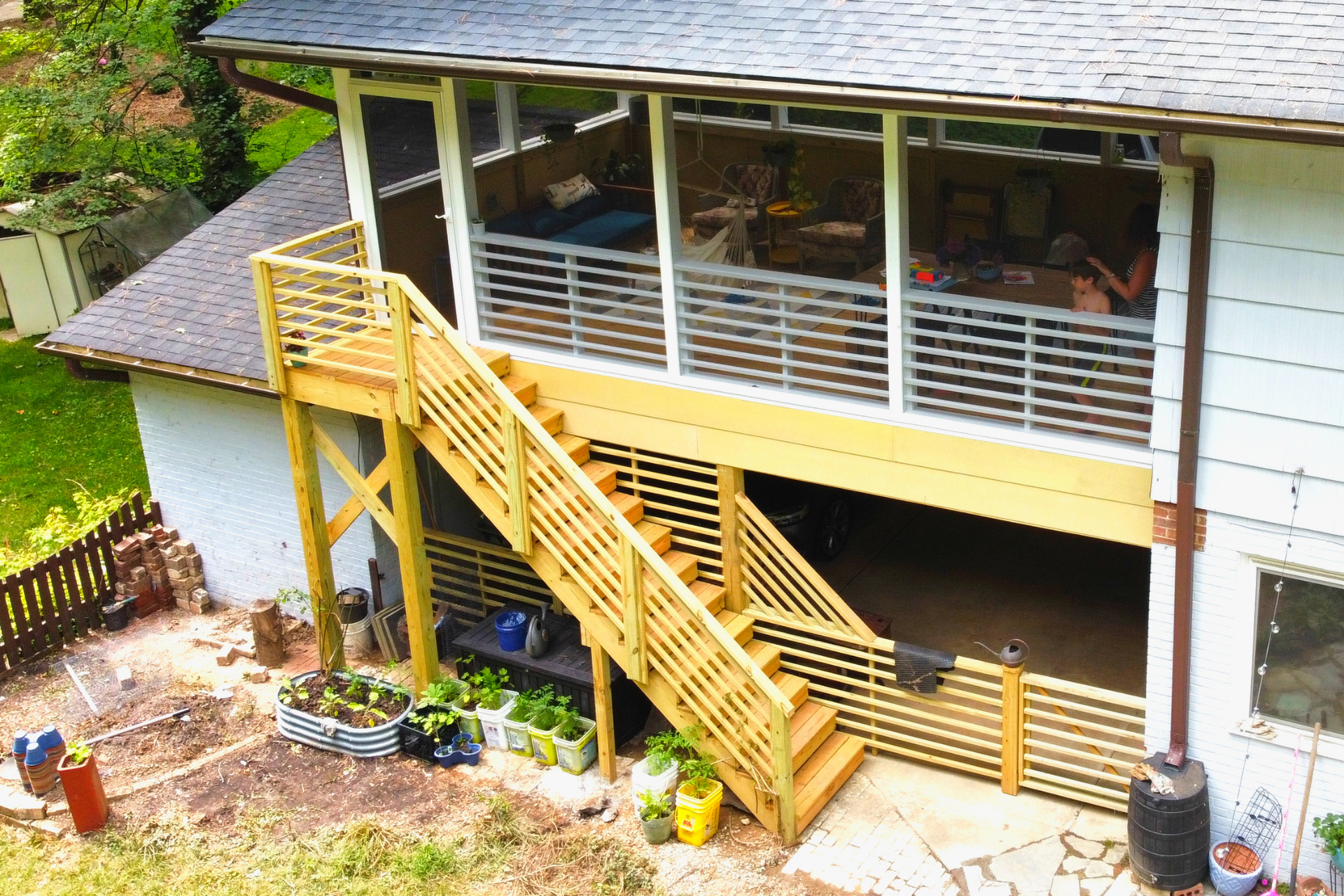 An elevated wooden deck with horizontal railings and a staircase leading down to a paved patio area next to a house.