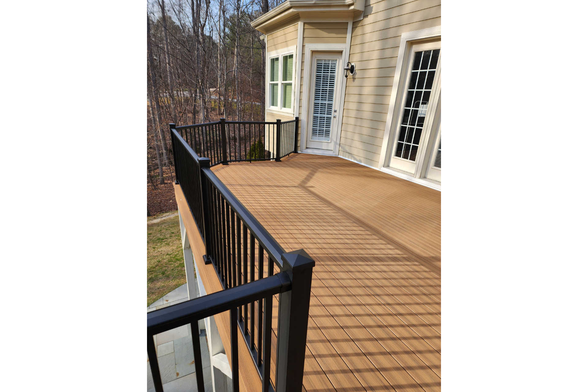 A beige deck with black railings overlooking a wooded area next to a multi-story house.