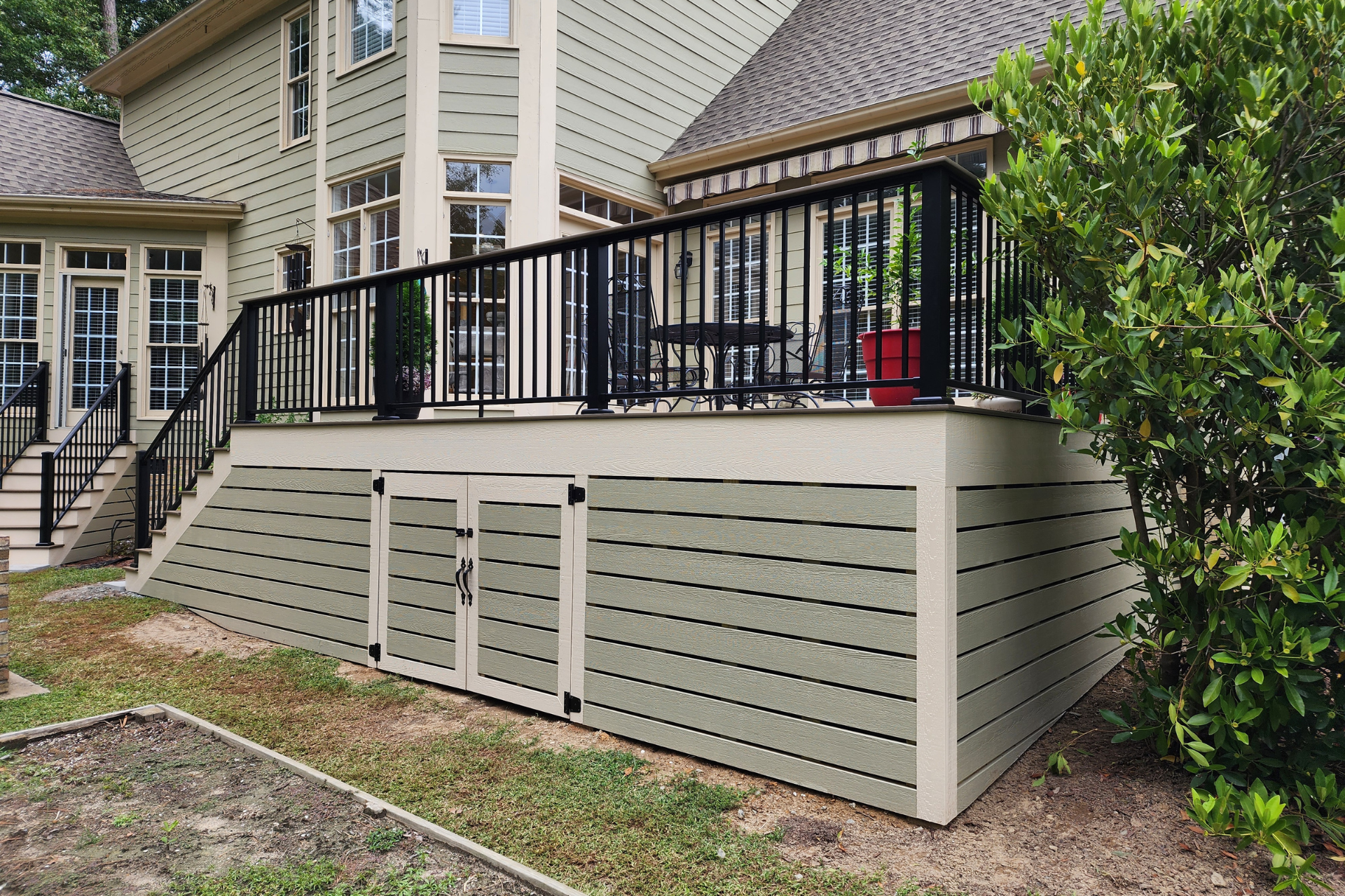 A residential deck with black metal railings and beige horizontal slat skirting, featuring a built-in storage door.