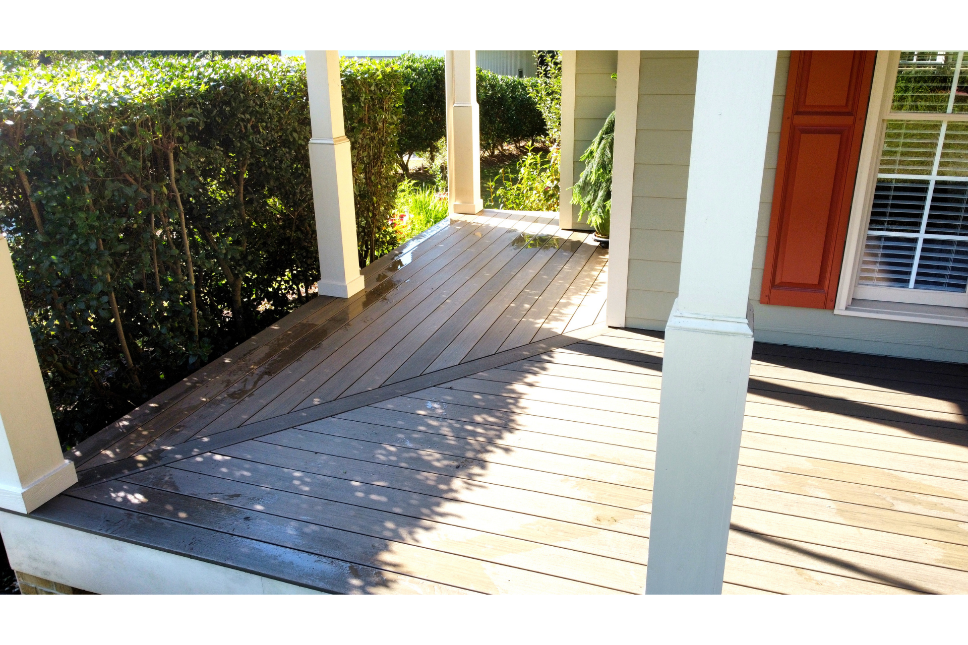 A wooden wheelchair ramp leading up to a house porch, positioned beside a green hedge.