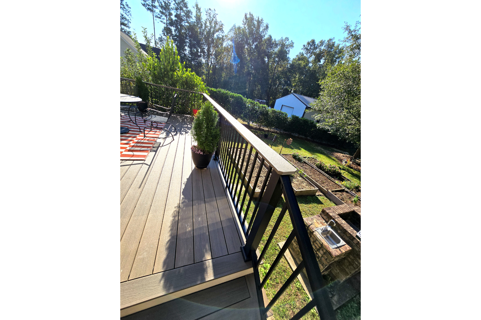 A wooden deck with a black railing overlooks a grassy backyard with trees, a stone fire pit, and a small shed.