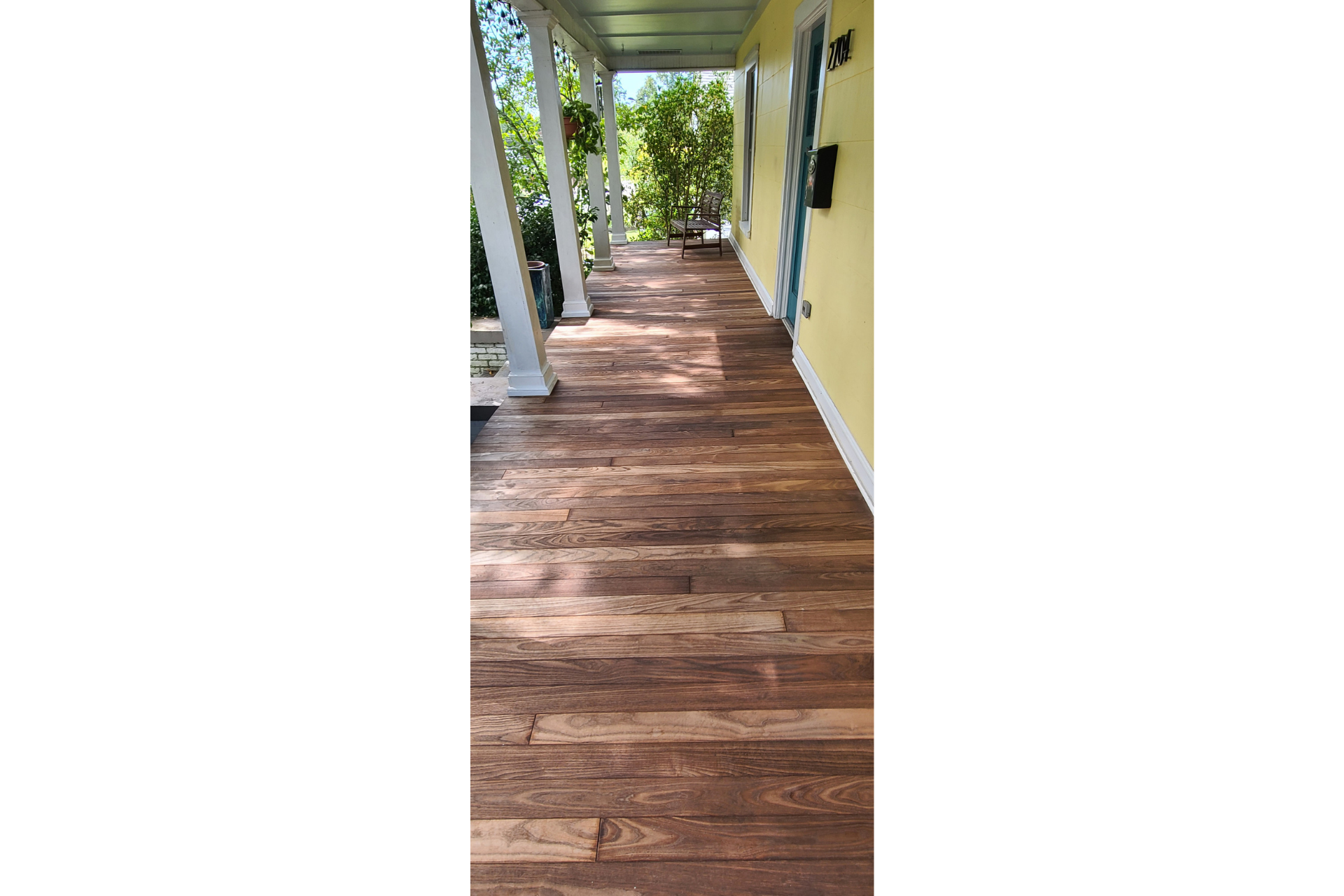 A wooden porch floor extends from the foreground toward a yellow building wall under a covered roof with white pillars.