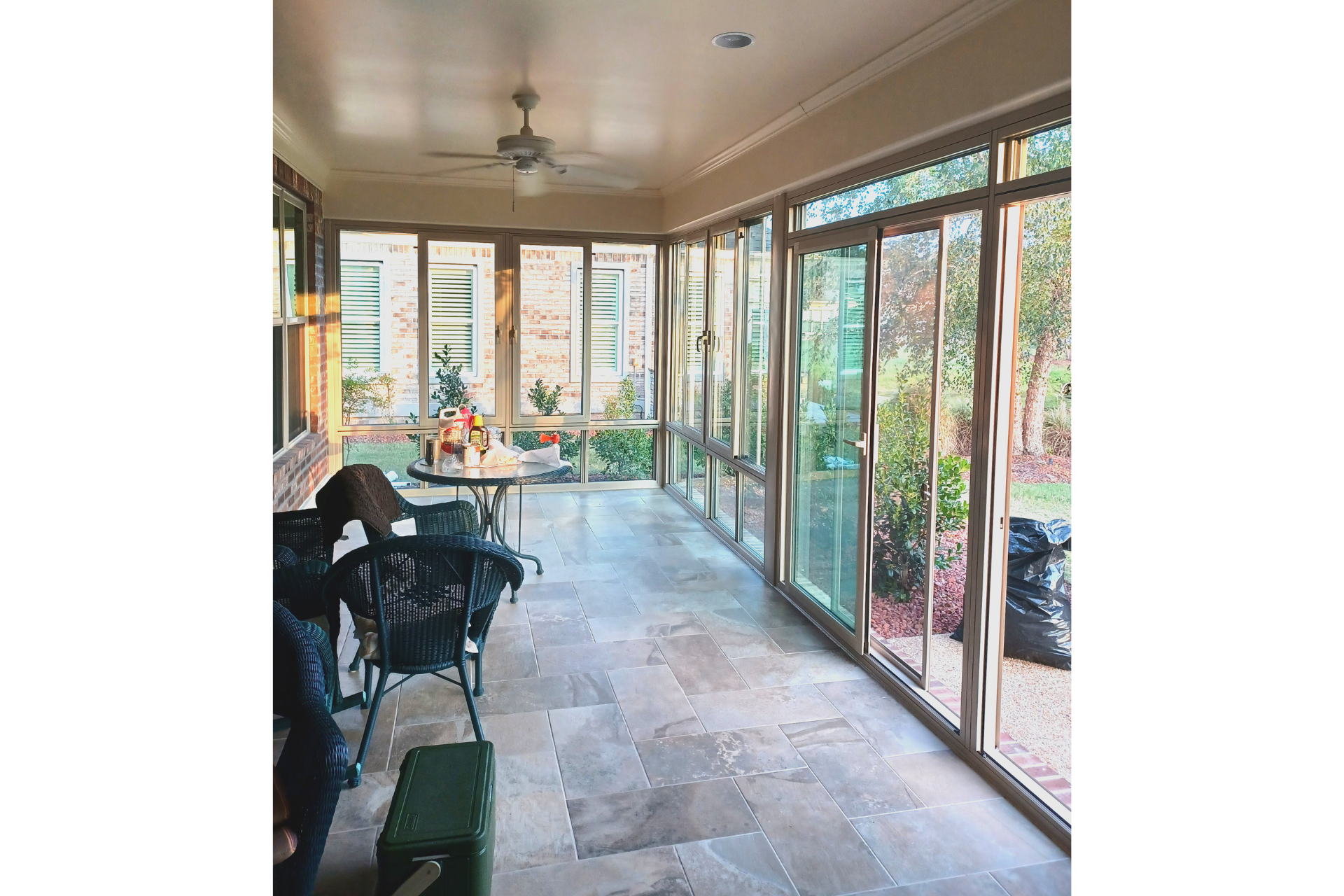 A sunroom with large windows, light tile floors, a ceiling fan, a small dining set, and some furniture.