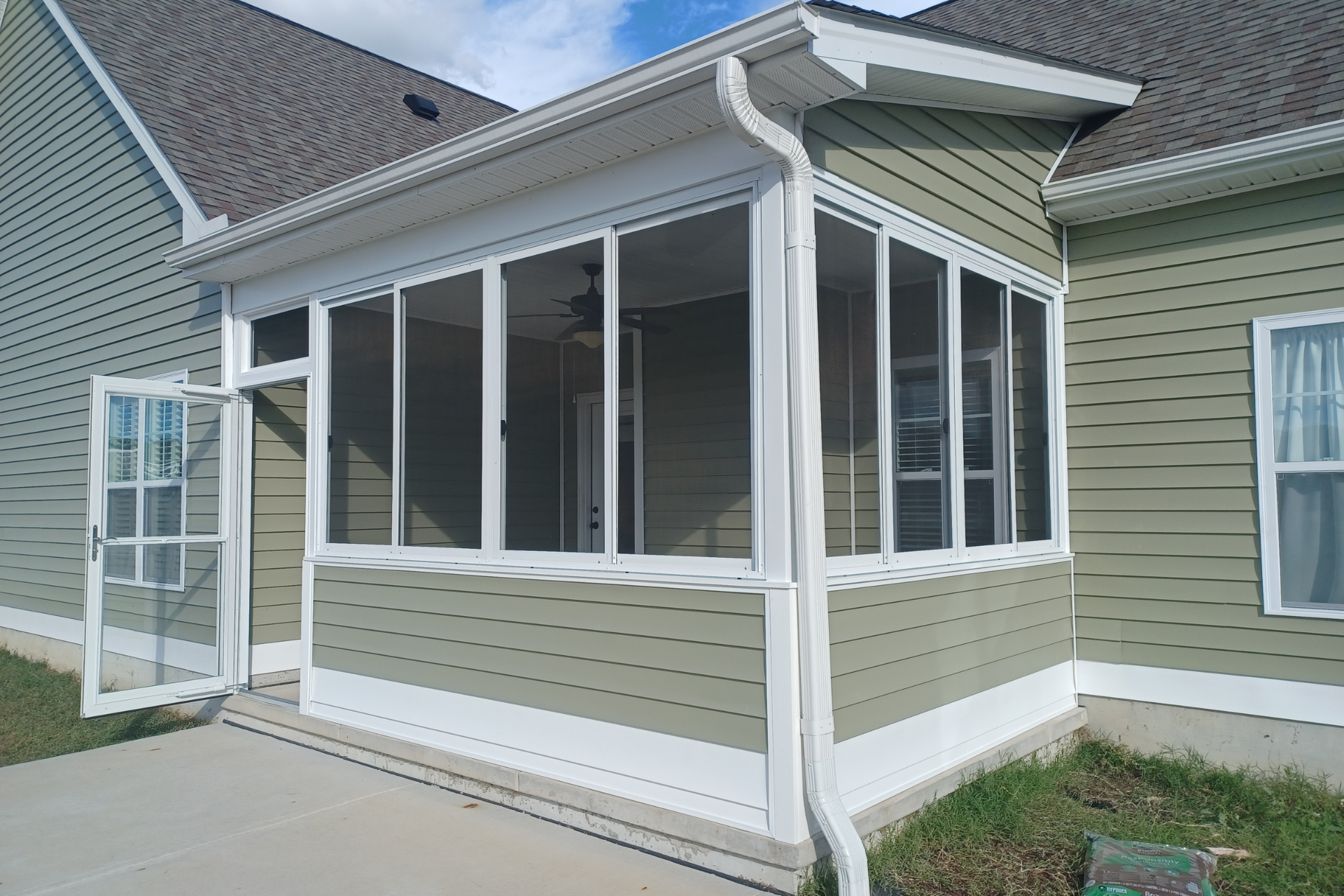 A green-sided house featuring an attached sunroom with white trim, large sliding windows, and an open screen door.