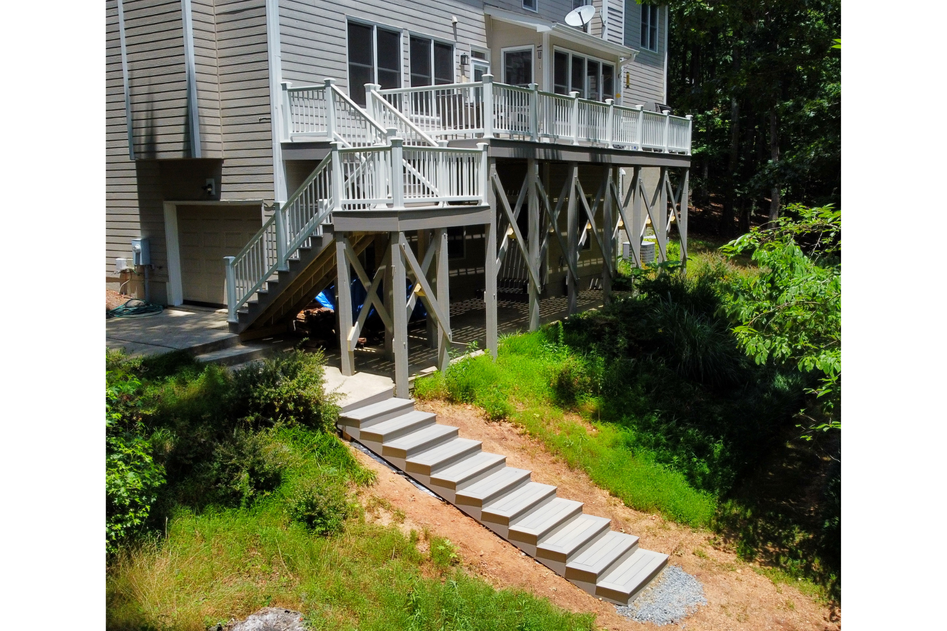 A tan house with a large white deck and stairway leading down to a long, tiered stone staircase on a grassy hill.