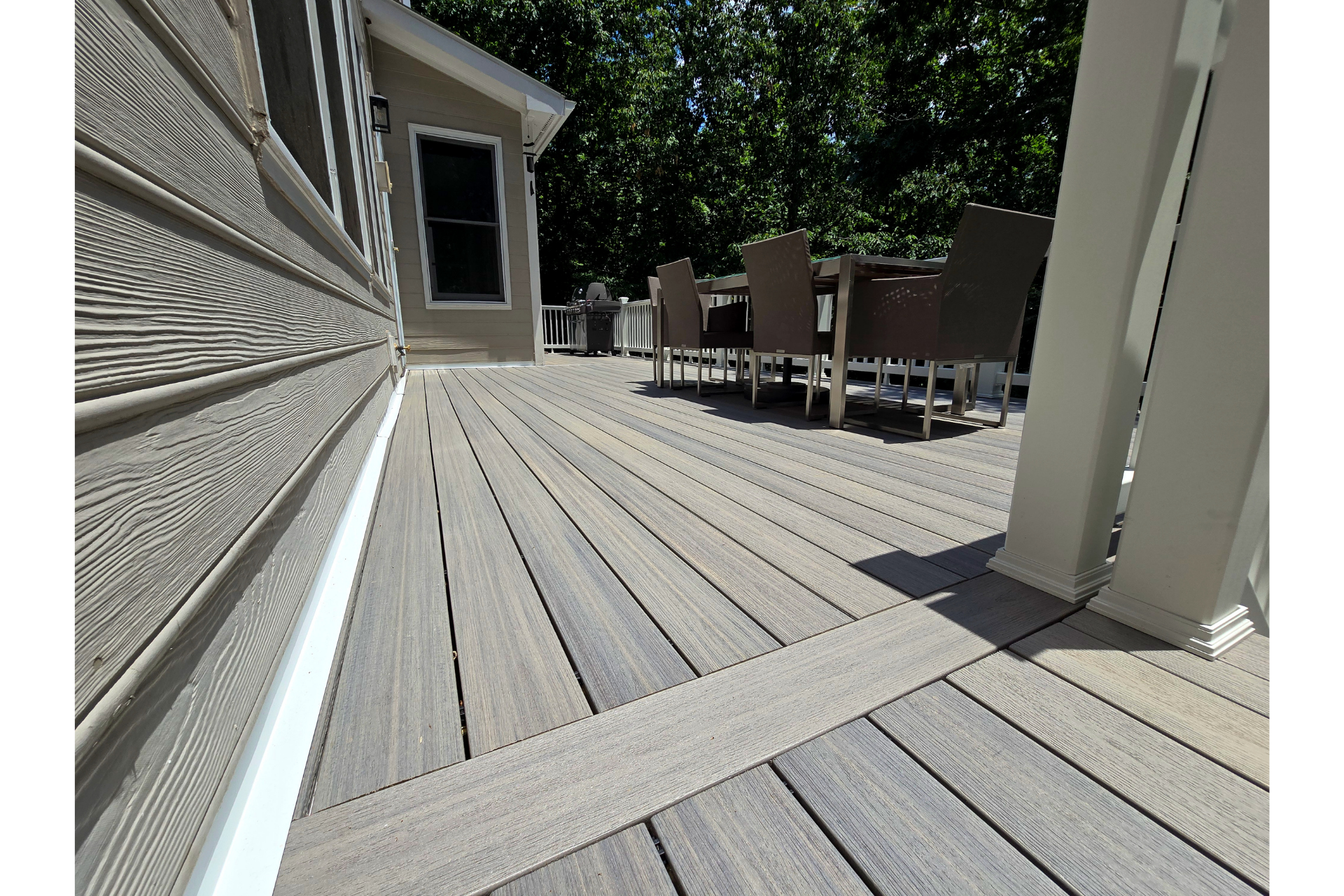A modern gray composite deck with a horizontal inlay border, adjacent to a house with light tan horizontal siding.