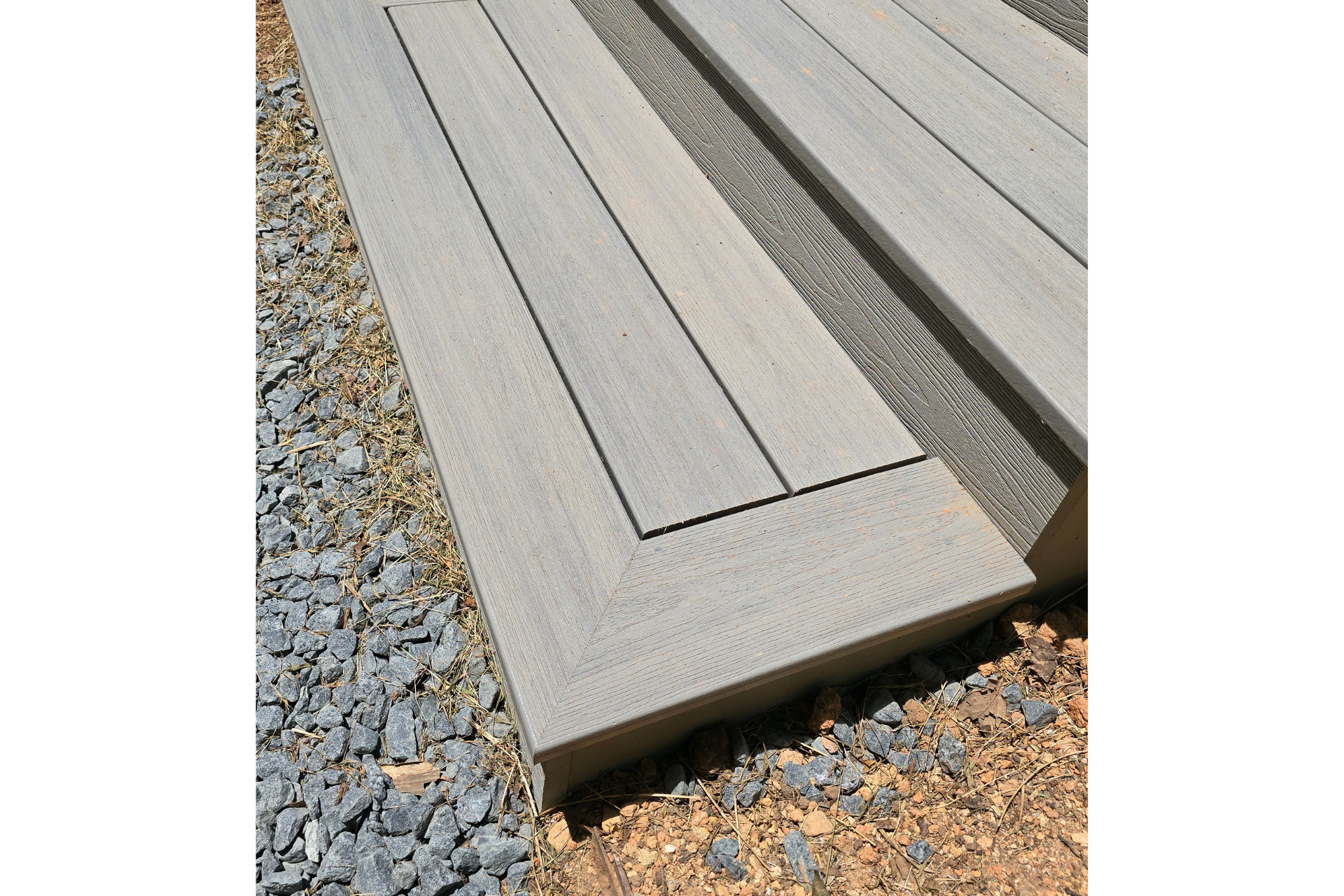 Two light gray composite deck steps with a border frame design, installed outdoors over gravel.
