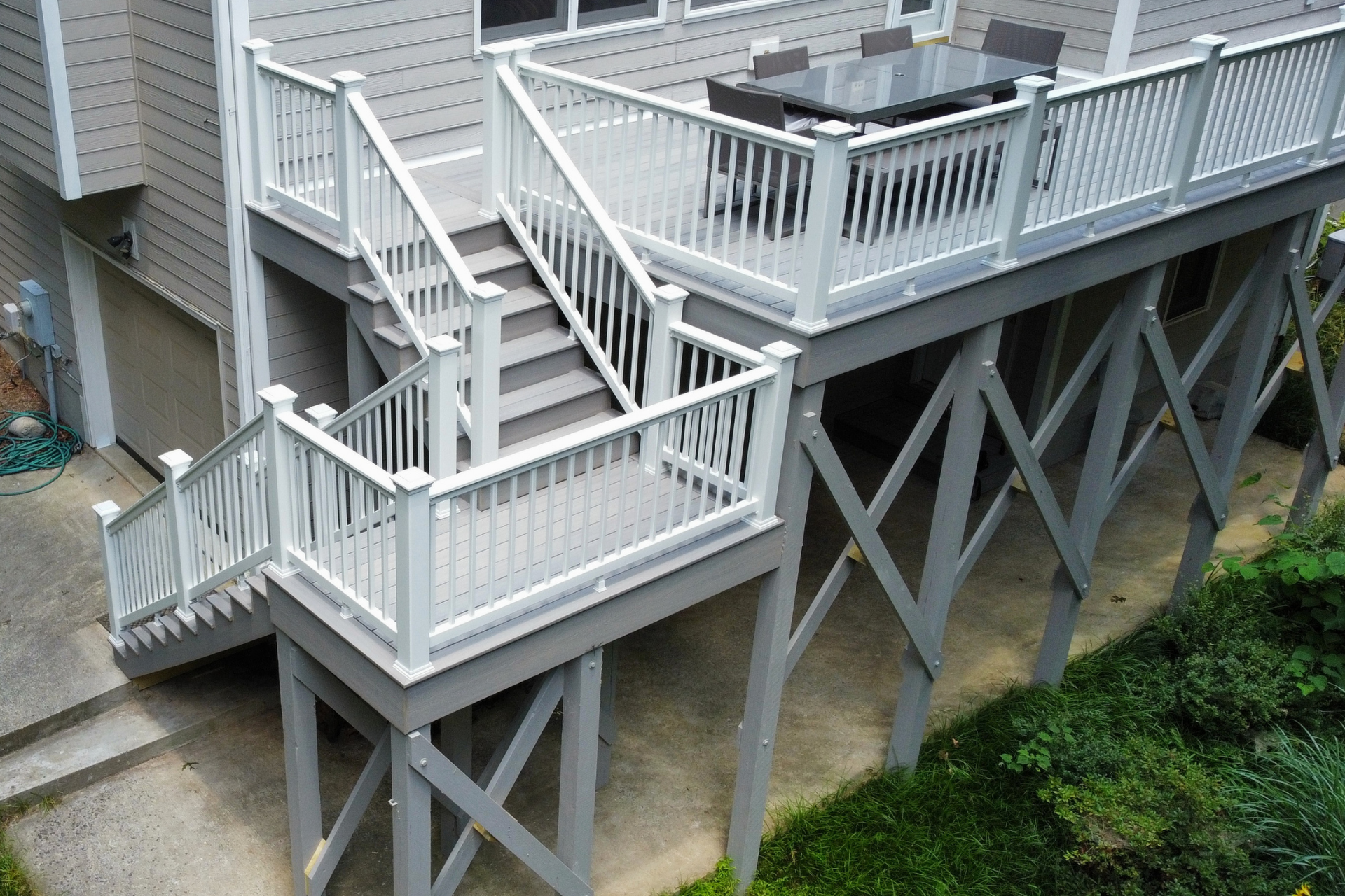 An elevated gray wooden deck with white railings and a staircase leading down to a concrete patio.