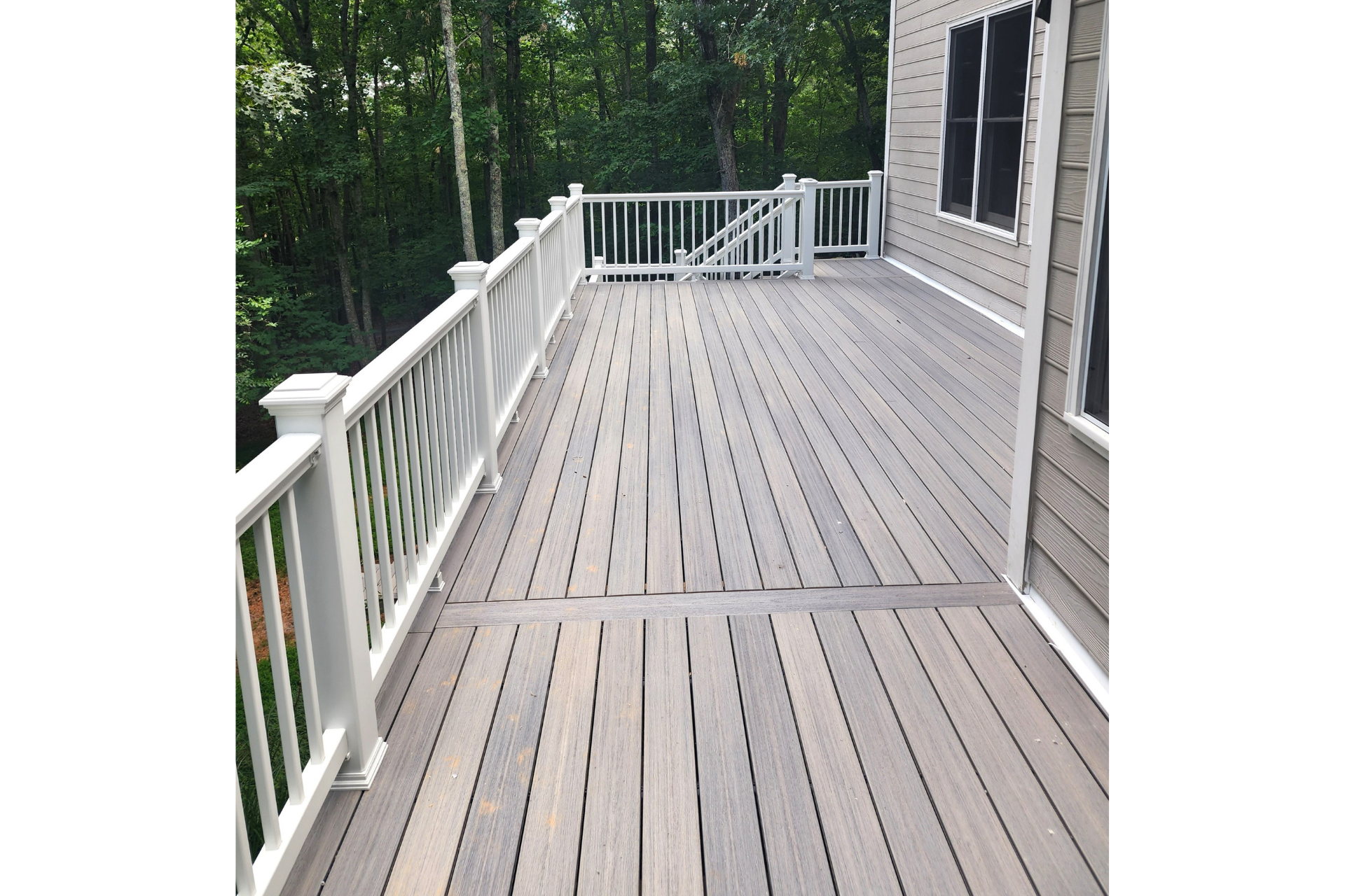 A high deck with gray composite boards, white railings, and a view of trees in the background.