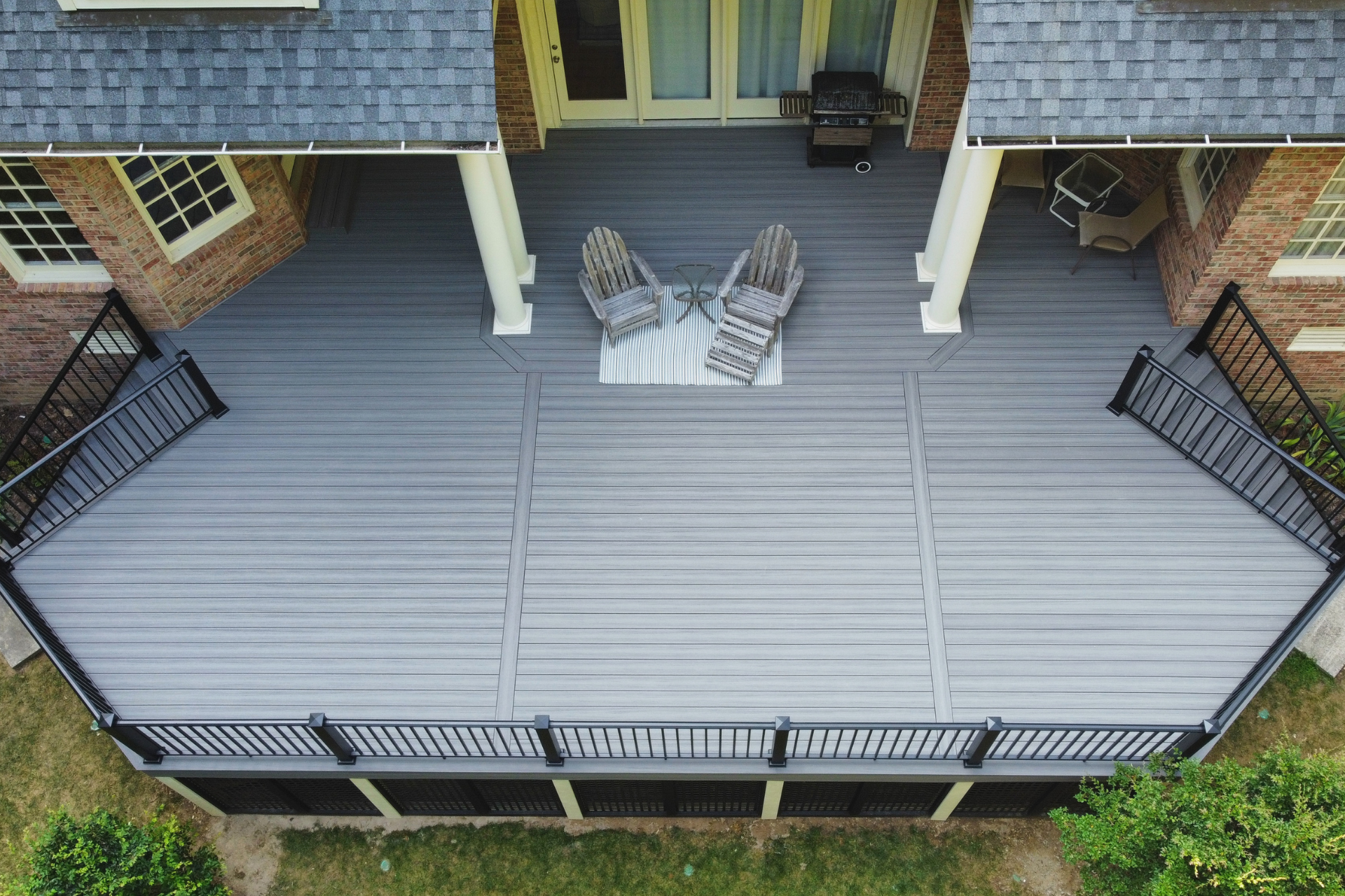 An elevated, grey composite deck with black railings and a two-chair seating area, viewed from above.