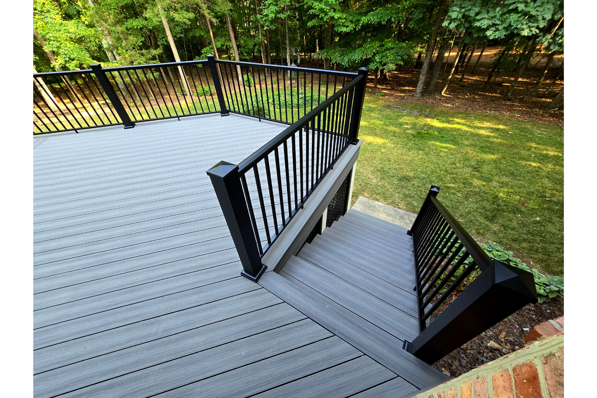 A high-angle view of a gray composite deck with black railings and stairs leading down to a green backyard.