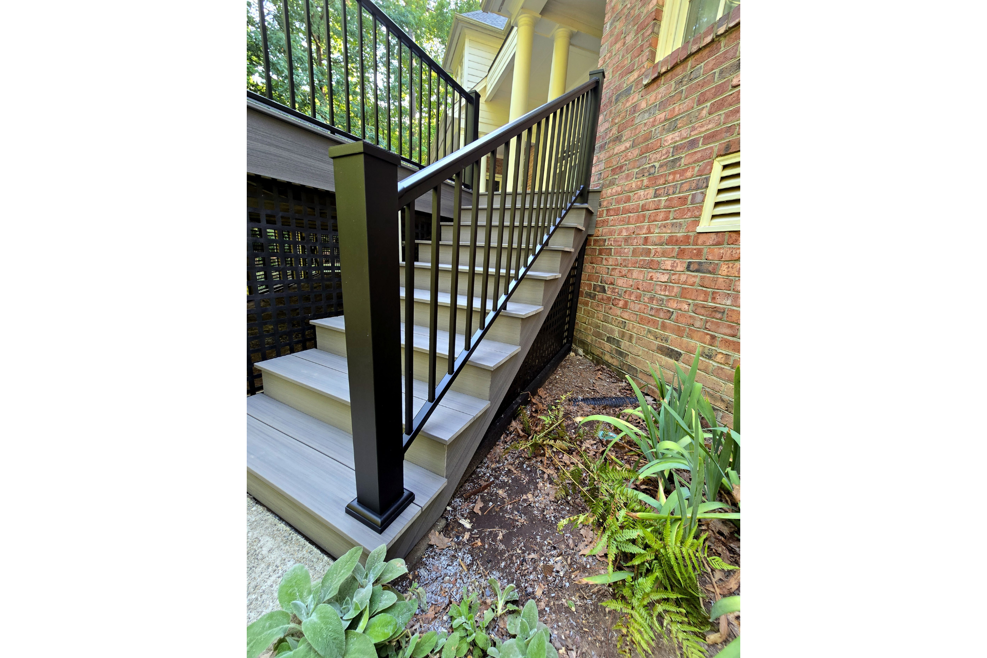 A set of gray stairs with black railings leading up to a wooden deck next to a brick house.