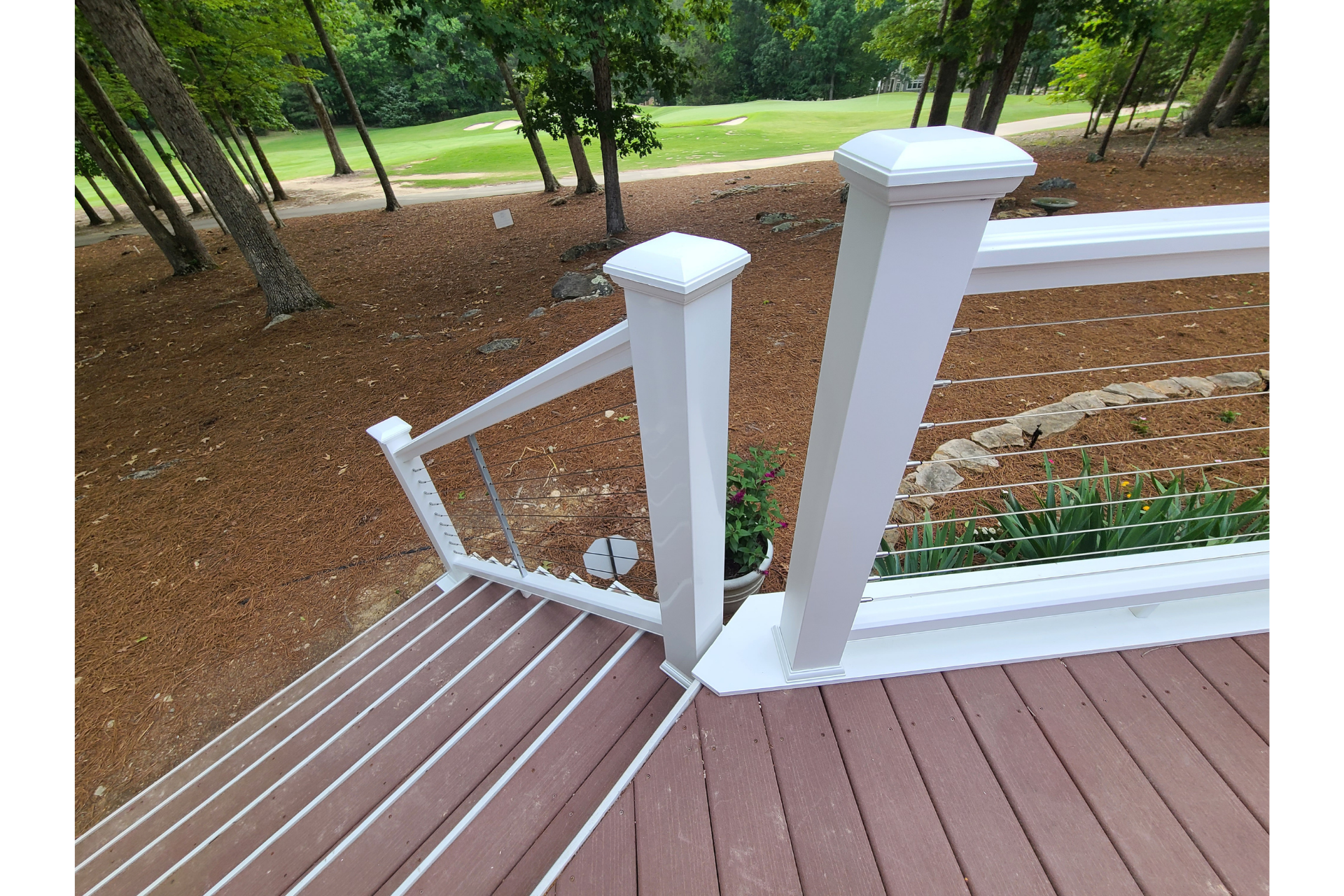 White deck railings with horizontal cable infill and square posts overlooking a grassy area with trees.
