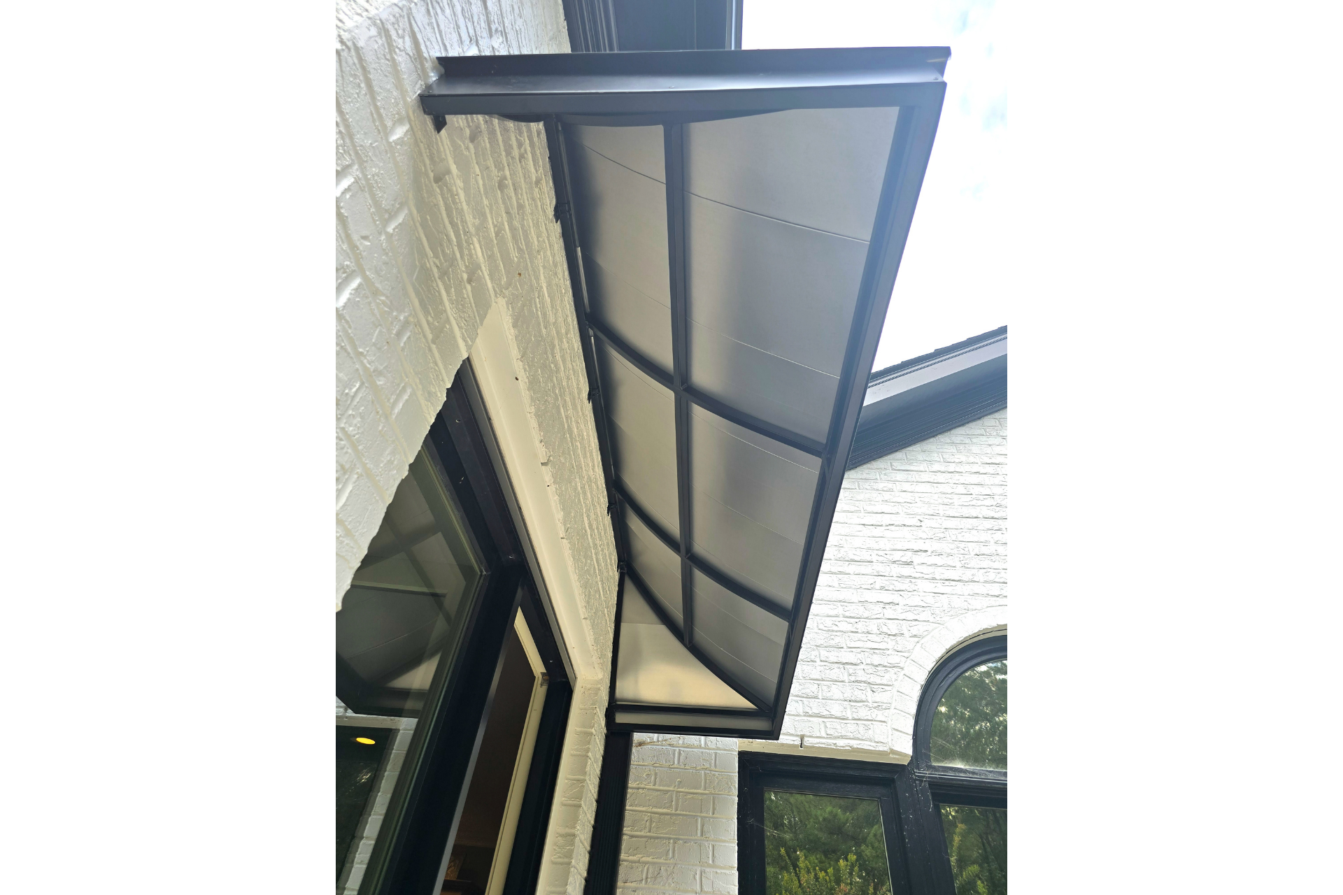 A modern black metal awning extends over a doorway, mounted against a white brick exterior wall.