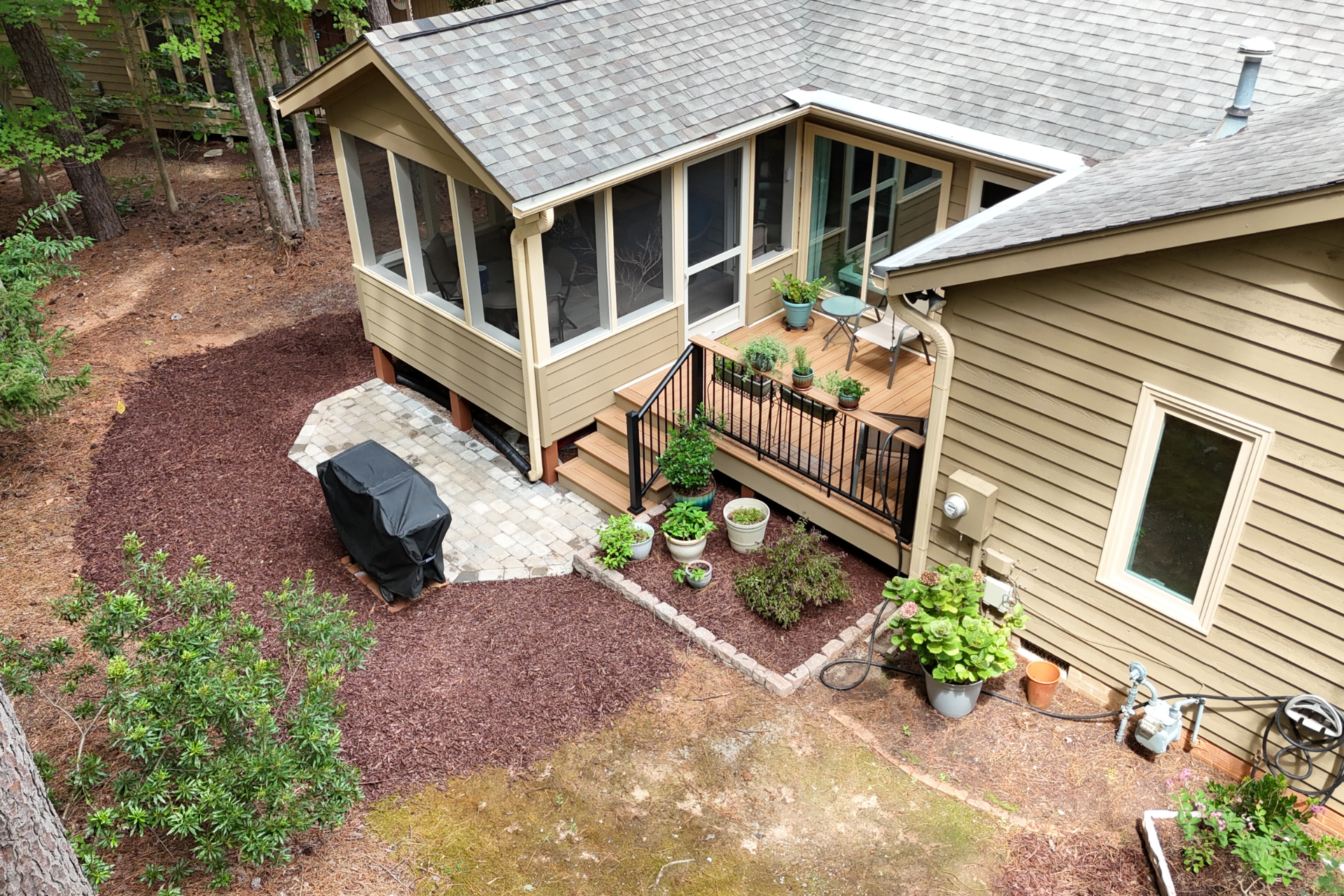 High-angle view of a tan house with a screened-in porch, wood deck, and a patio area covered in dark wood mulch.