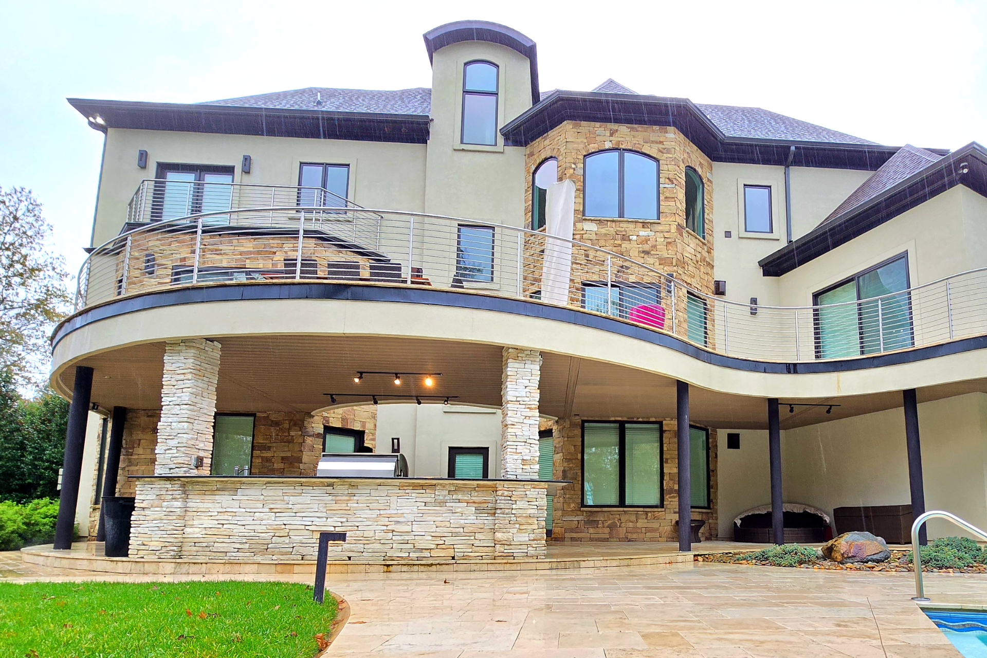A two-story home with a stone-accented exterior, a curved patio, an outdoor bar area, and a swimming pool.