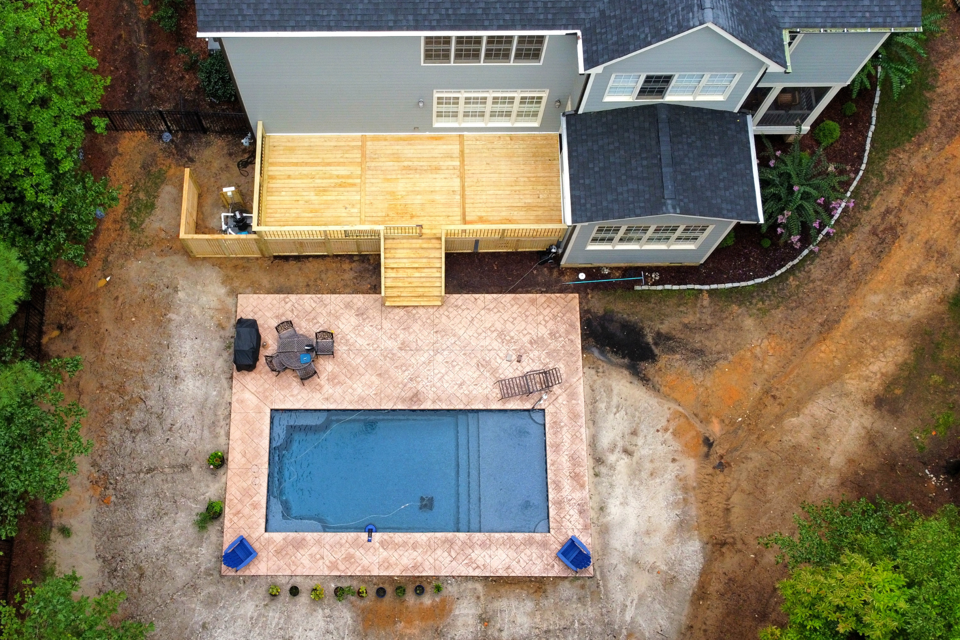 An aerial view of a gray house with a new wooden deck and a swimming pool surrounded by a stamped concrete patio.