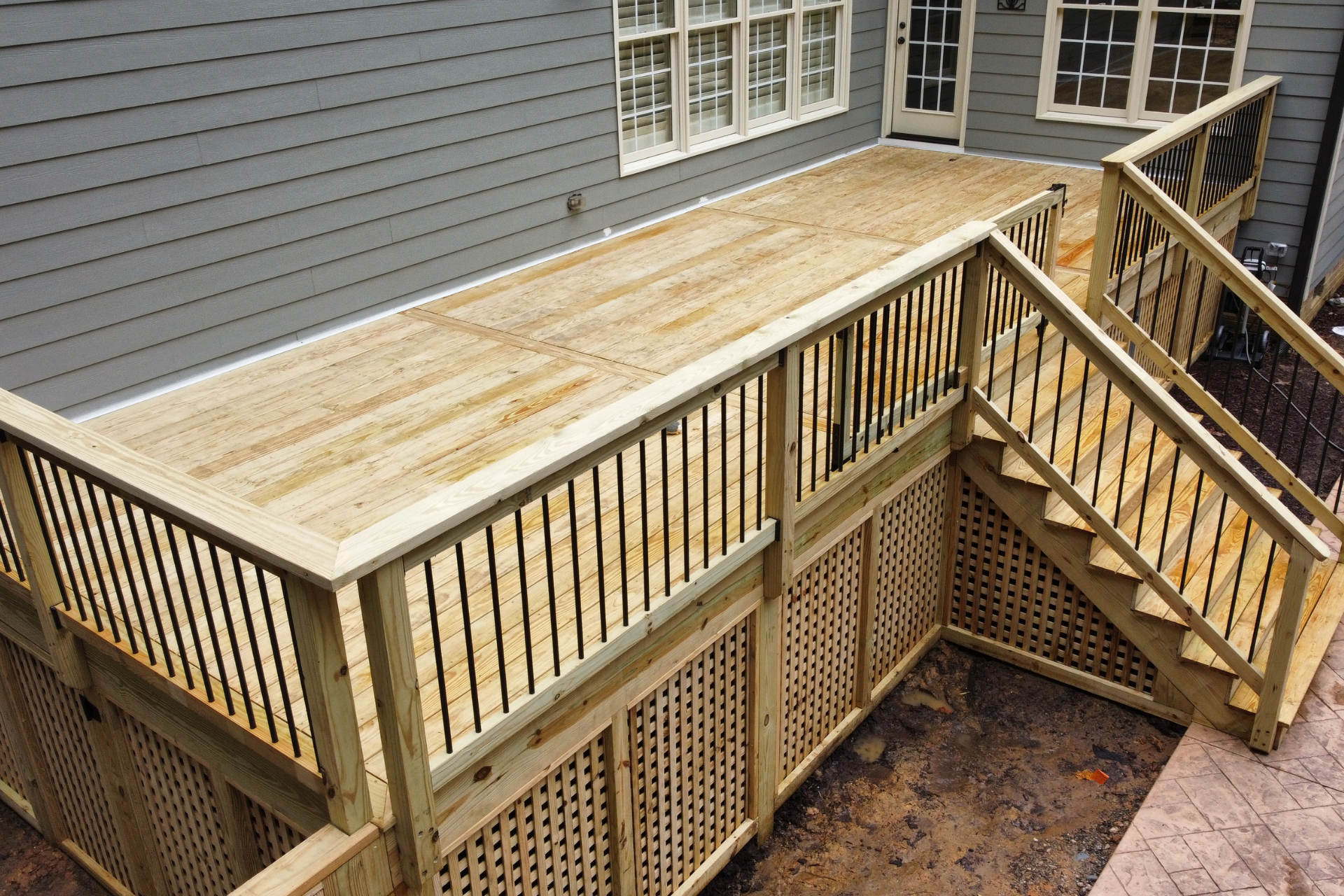 A newly built wooden deck with railings and stairs attached to a house with gray siding and lattice skirting underneath.