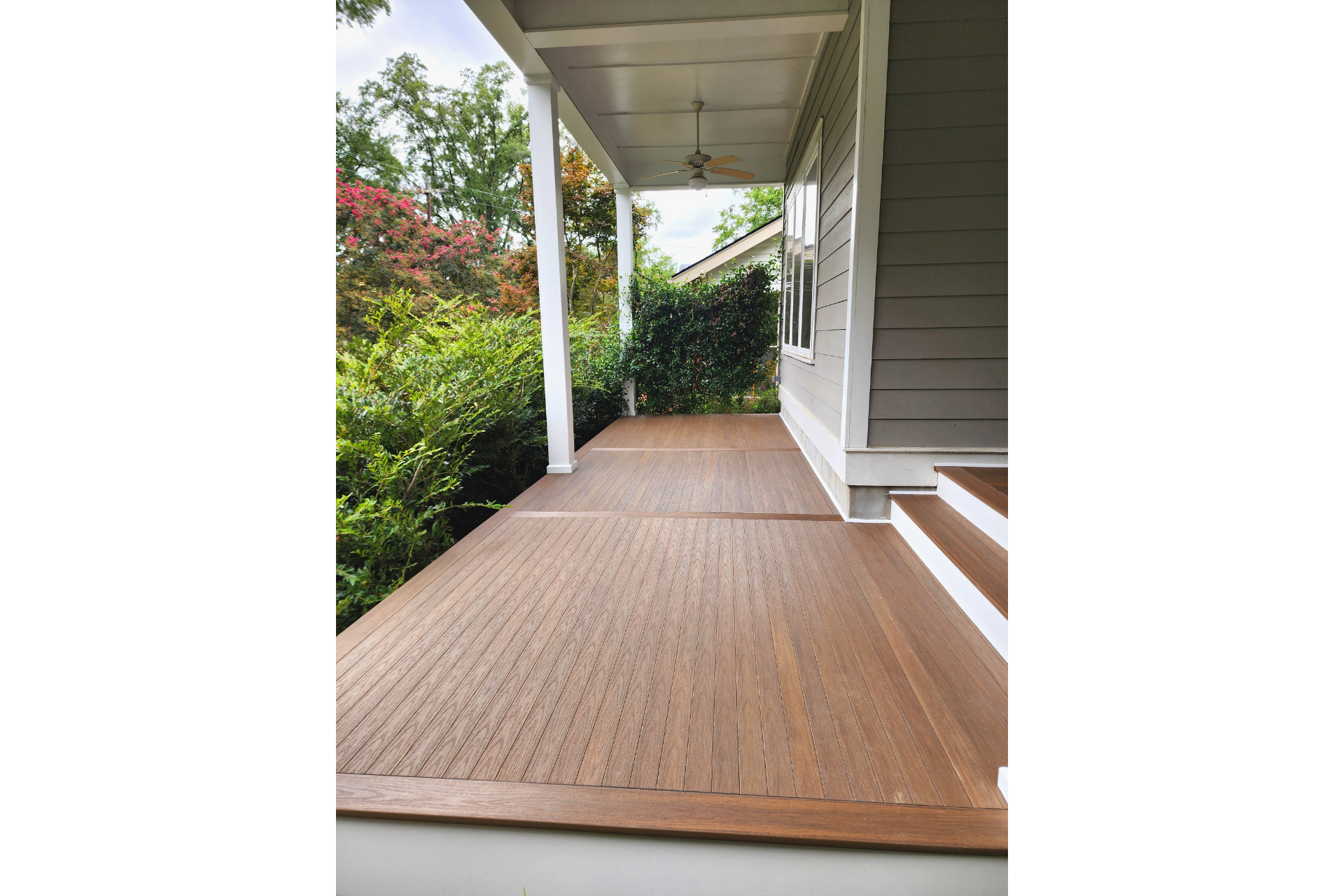 A light-colored wooden porch deck with a covered roof, white support posts, and steps leading up to the house exterior.