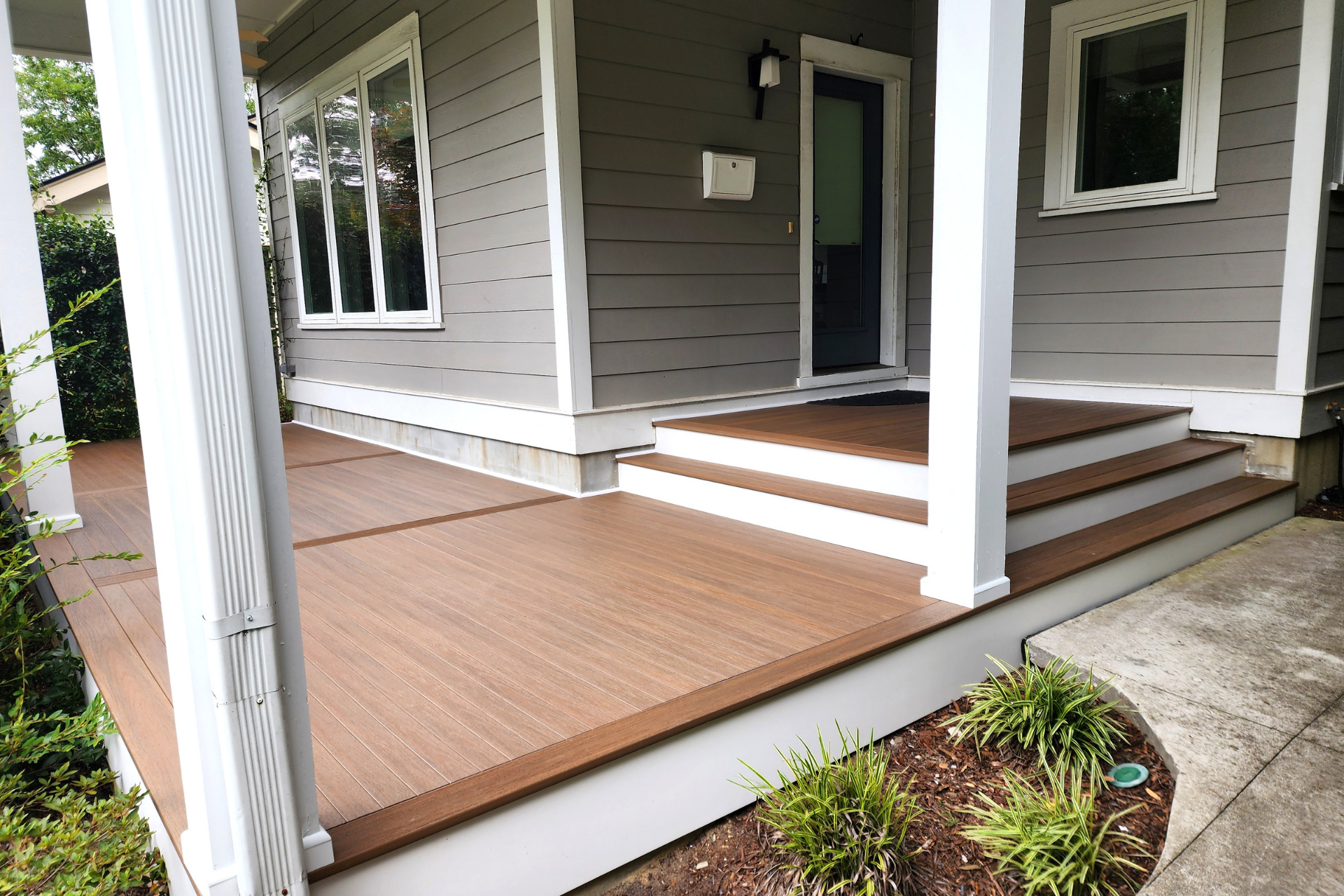 A newly renovated front porch with brown composite decking and white posts and trim leading to the house entrance.
