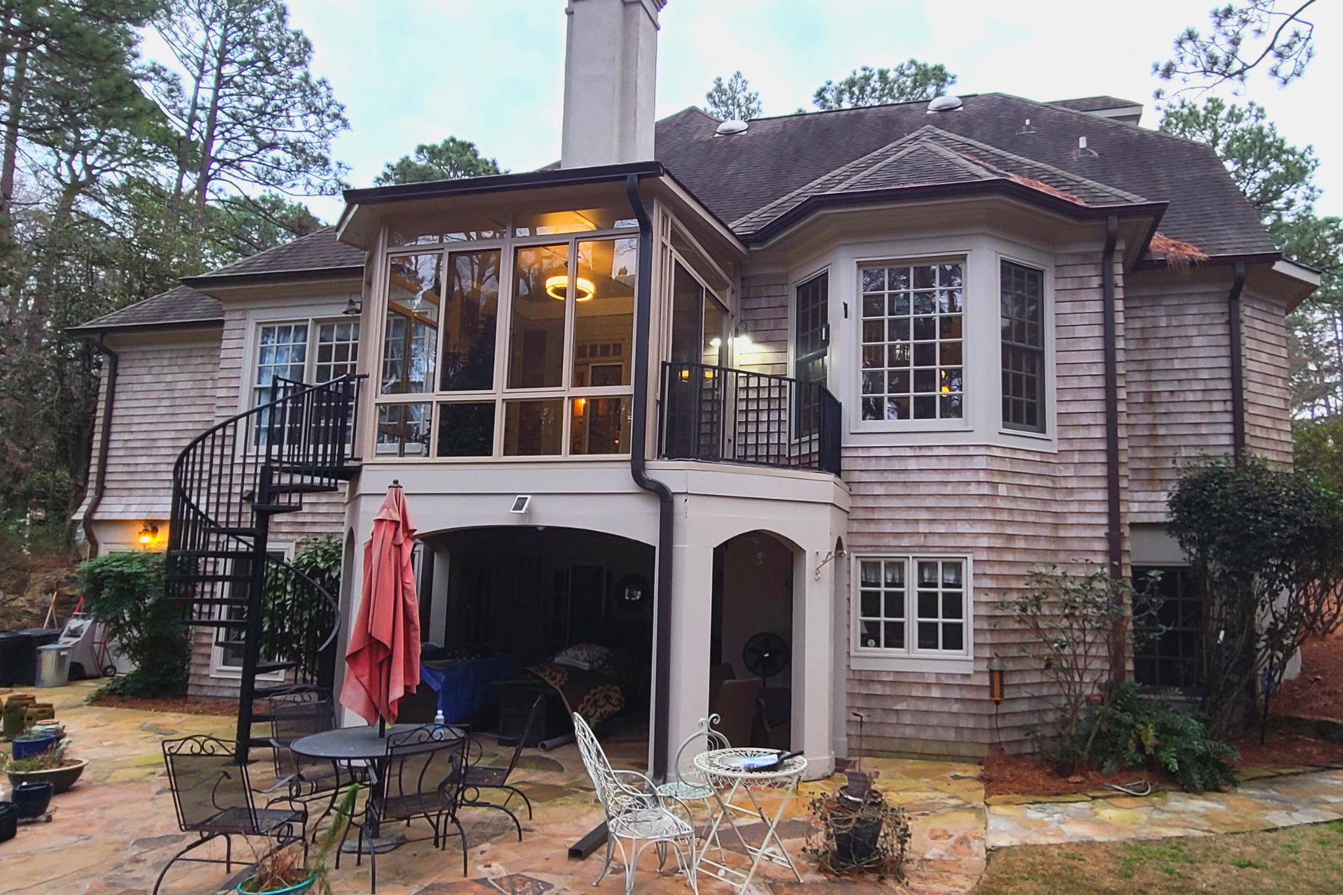 Backyard view of a two-story home with light stone siding, a spiral staircase, an elevated porch, and a patio area.