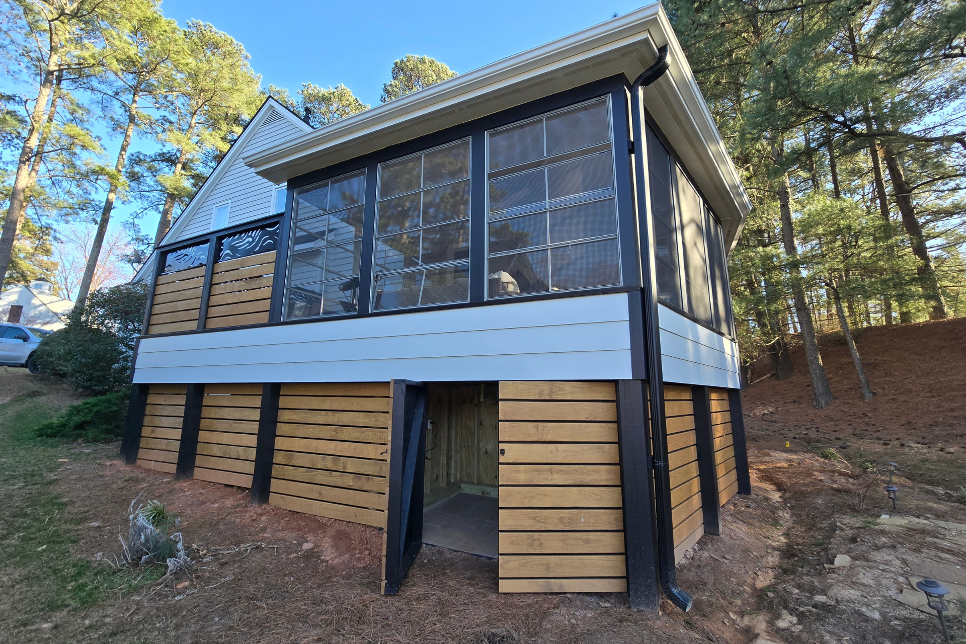 A two-story deck with a screened upper level and horizontal wood slat skirting, situated in a wooded backyard.