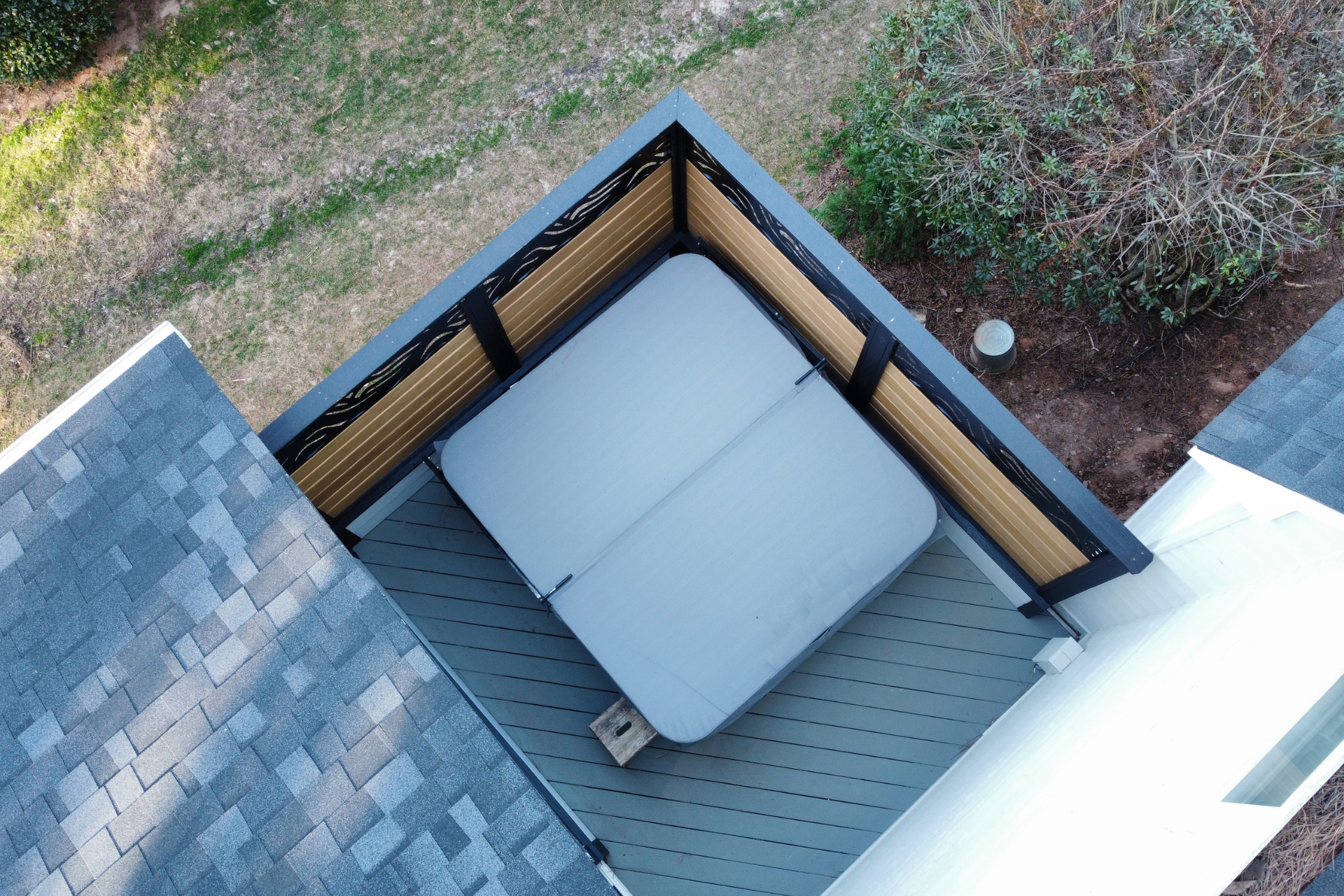 An overhead view of a square hot tub with a grey cover placed on a deck surrounded by wooden privacy fencing.