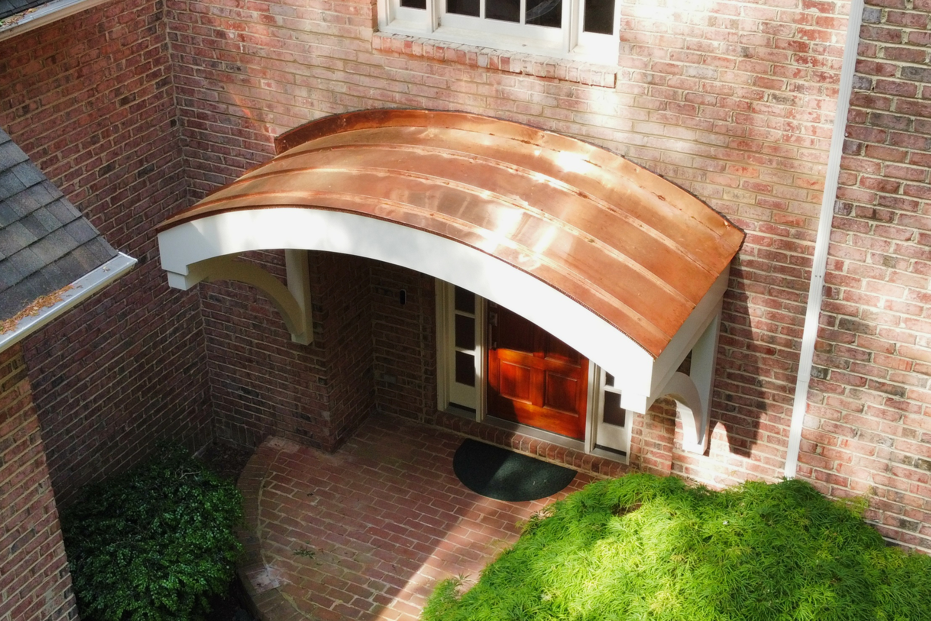 A curved copper awning over a wooden front door, set against a brick house exterior.