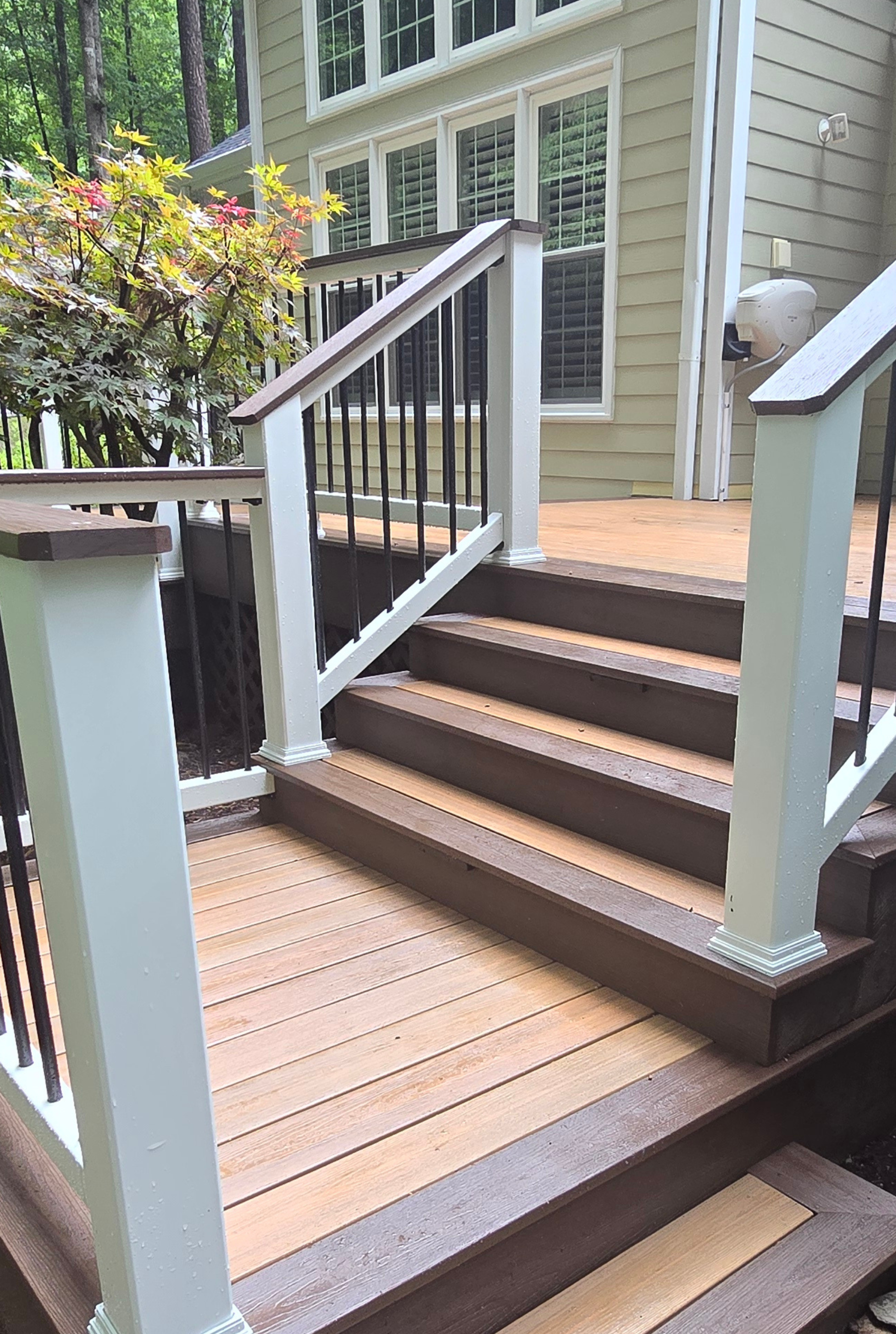Outdoor wooden stairs with tan planks and dark brown risers leading to a home deck with white railings.