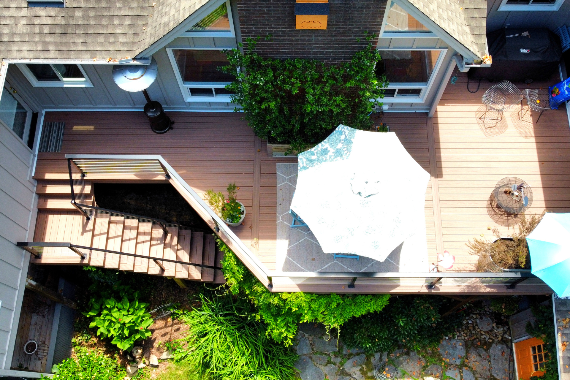 An aerial view of a wooden deck with stairs, a patio umbrella over a dining area, and lush green plants in the backyard.