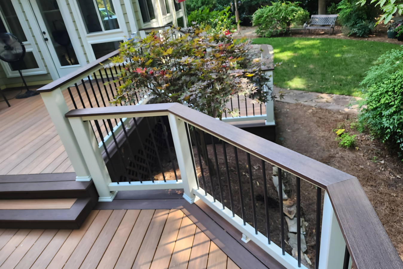 A high-angle view of a backyard deck with light brown composite boards, a multi-tiered staircase, and a wood-topped railing.