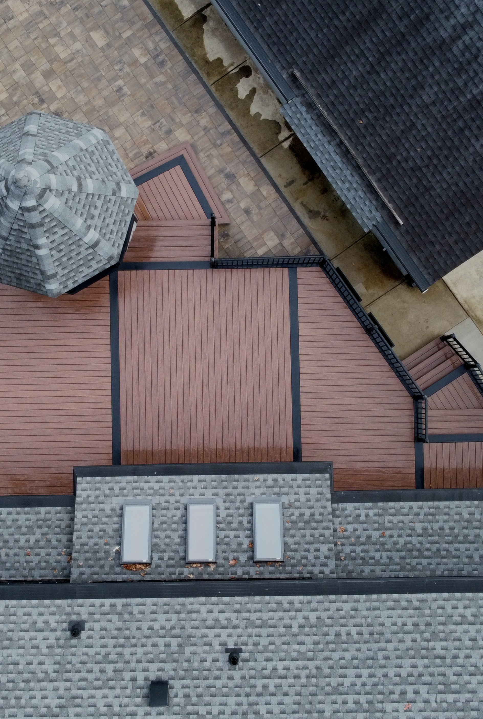 An aerial view shows a reddish-brown deck with dark borders, stone-tiled roof sections, and three rectangular skylights.