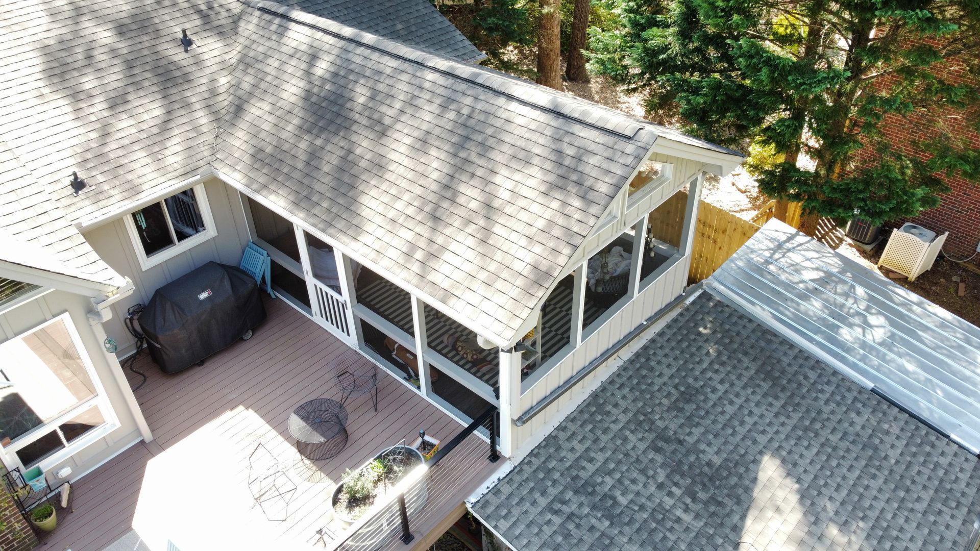 A high-angle view of a backyard with a screen-enclosed porch attached to a house, a deck, and an adjacent shingled roof.