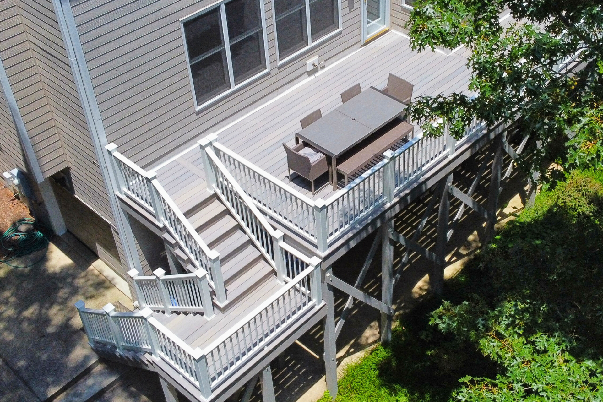 An elevated outdoor deck with a gray dining set, featuring a staircase leading down to a concrete ground level.