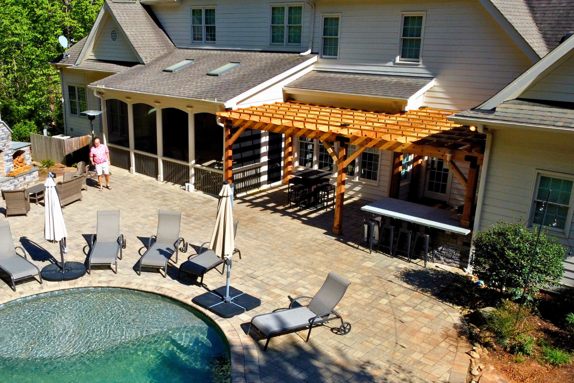 A backyard patio features a swimming pool, lounge chairs, a wooden pergola, and a covered porch attached to a house.