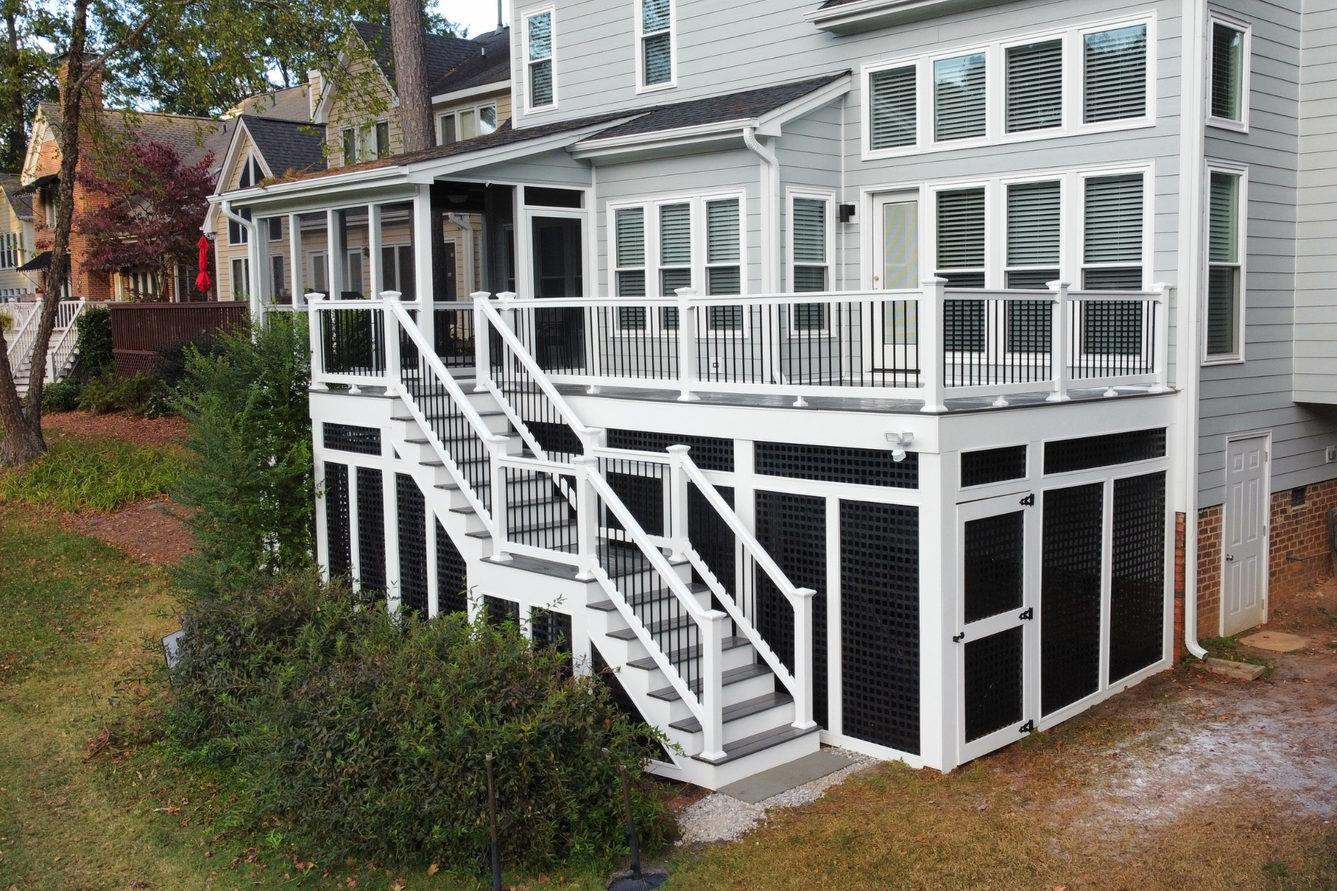 A light gray house features a elevated composite deck with white railings, stairs, and dark lattice skirting.