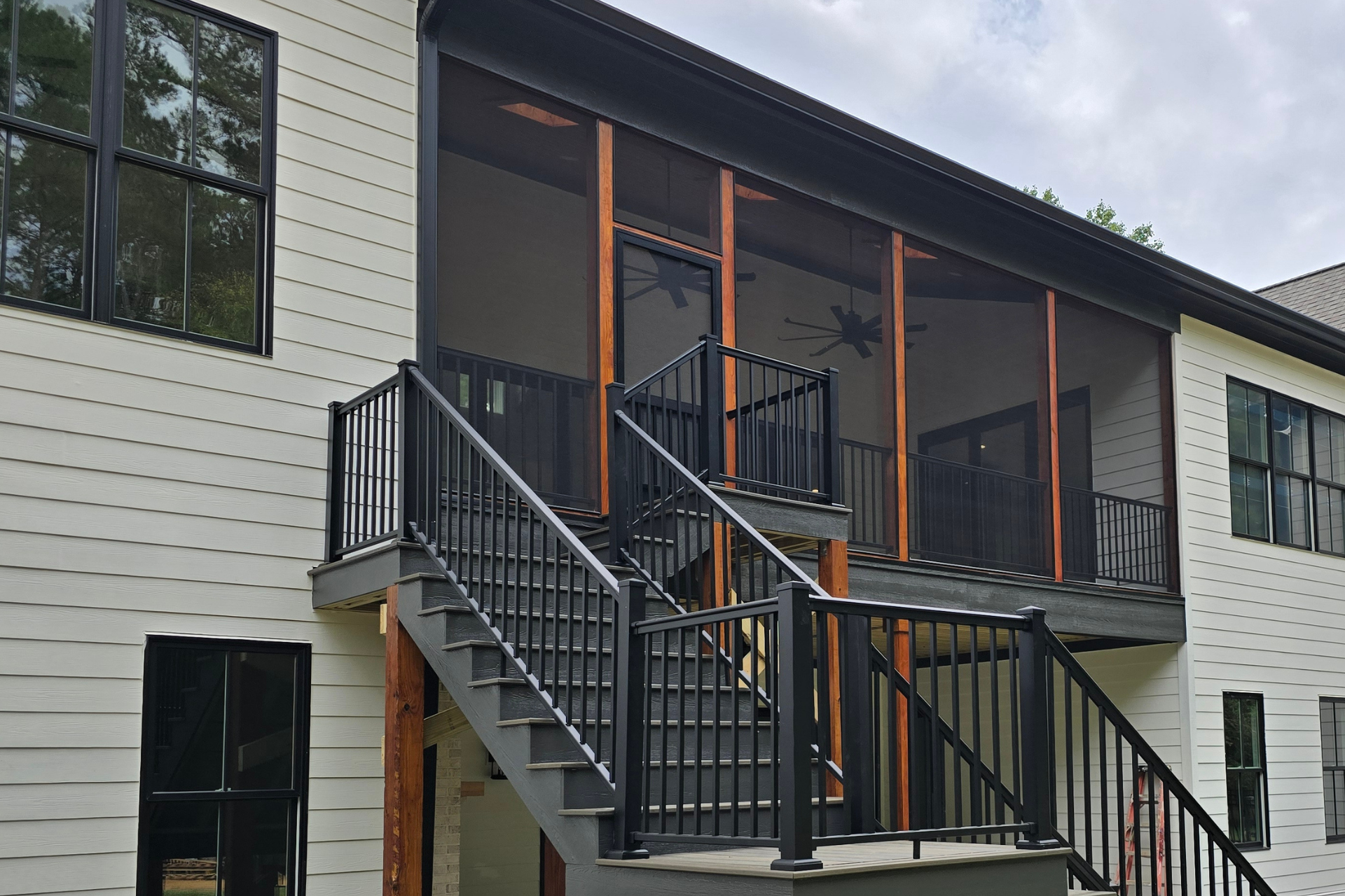 A cream-colored house with a large, two-story black screened-in porch and black metal stairs leading to a deck.