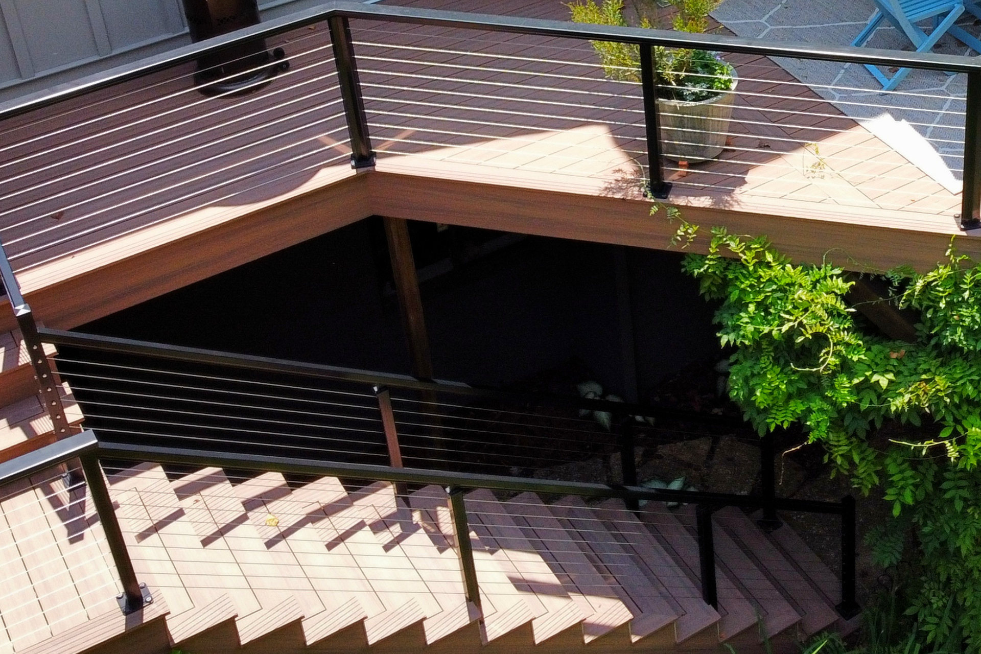 Wooden outdoor stairs leading down from a deck, featuring dark metal railings and a shaded, recessed lower landing area.