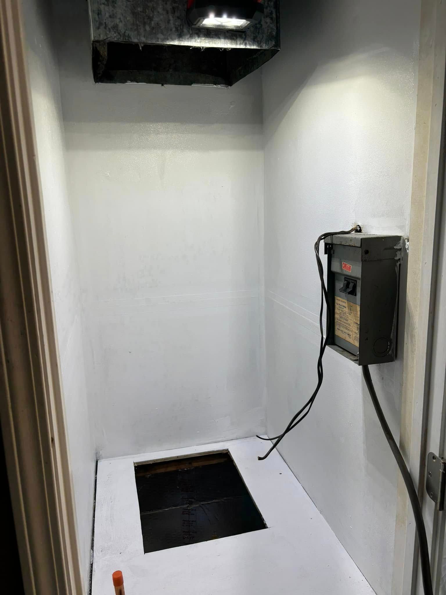 A small room with a hole in the floor and a heater on the wall.