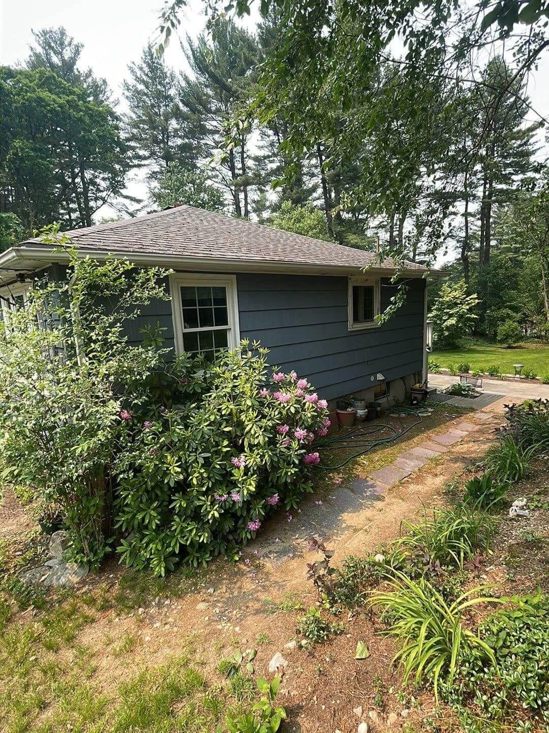 A small house with a roof that is surrounded by trees and bushes.
