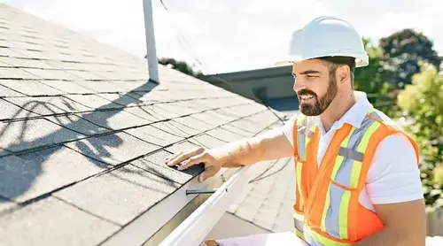 A construction worker is working on a roof with a drill.