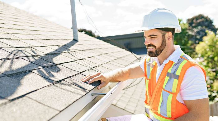 A man is standing on top of a roof looking at the shingles.