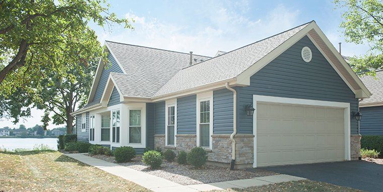 A blue house with a white garage door is next to a lake.