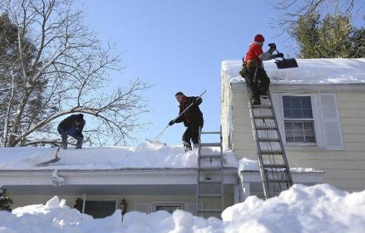 A group of people are clearing snow from the roof of a house
