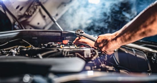 Un uomo sta lavorando al motore di un'auto con una chiave inglese.