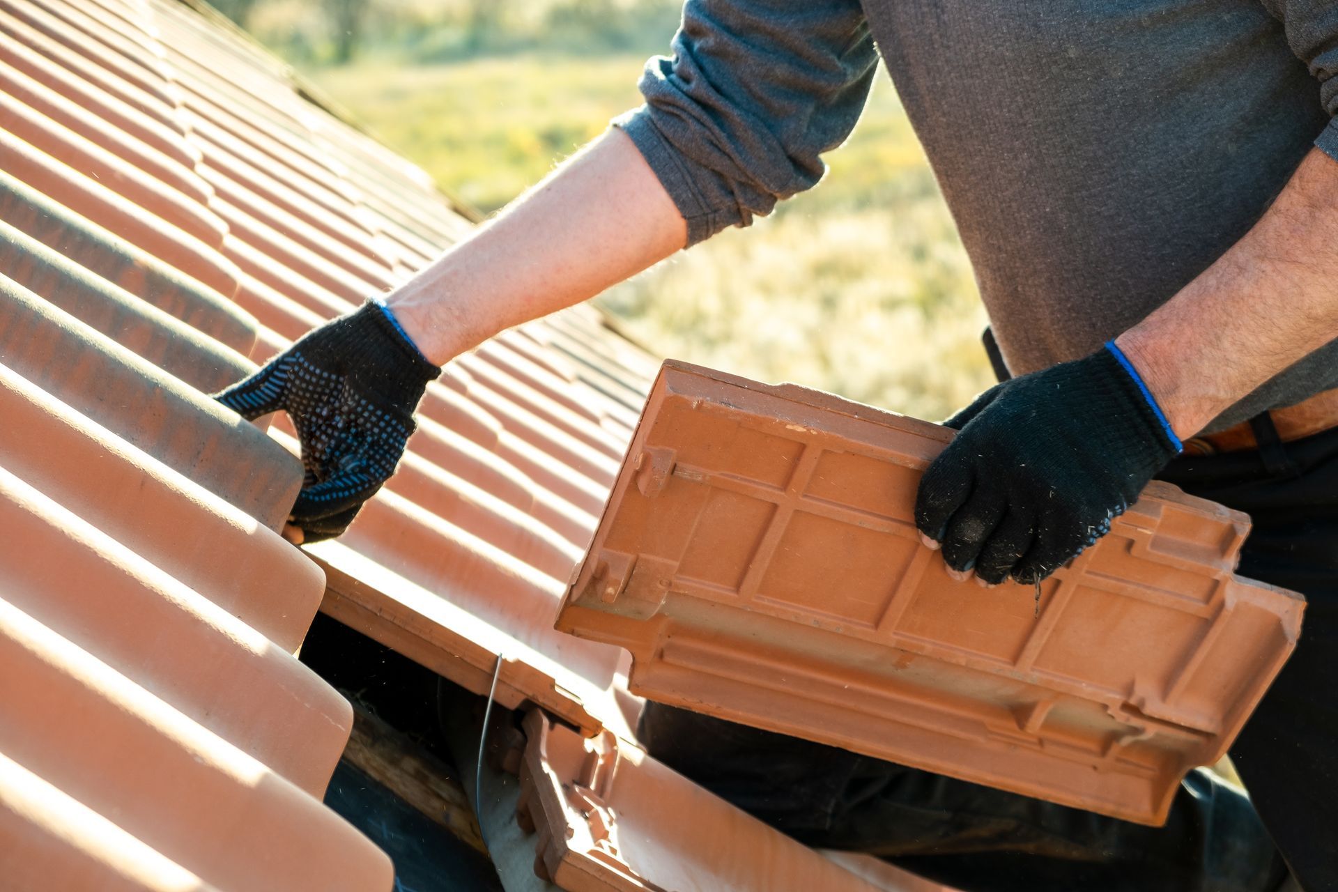 Gloved worker installing terracotta roof tiles on a sloped roof