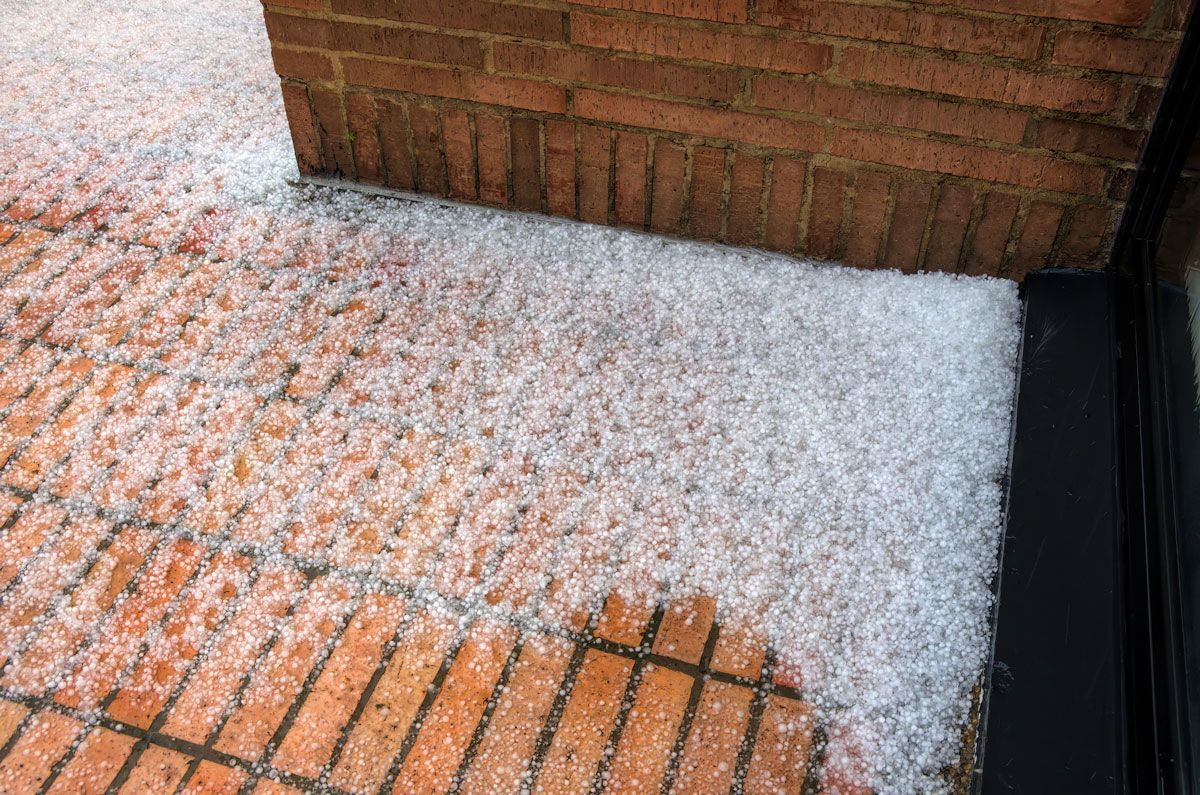 There is a lot of hail on the ground near a brick wall — Holmen, WI — Riverland Exteriors Corporation
