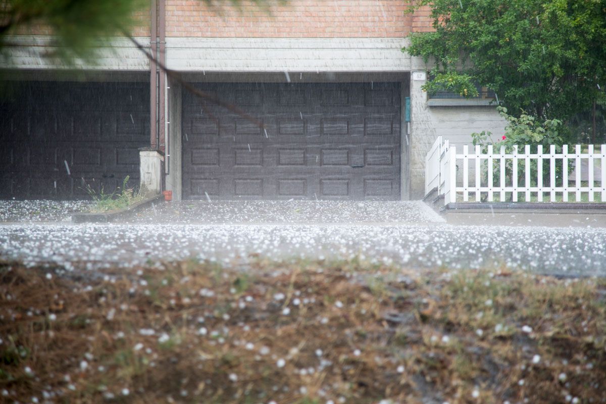 There is a lot of hail on the ground in front of a garage door — Holmen, WI — Riverland Exteriors Corporation